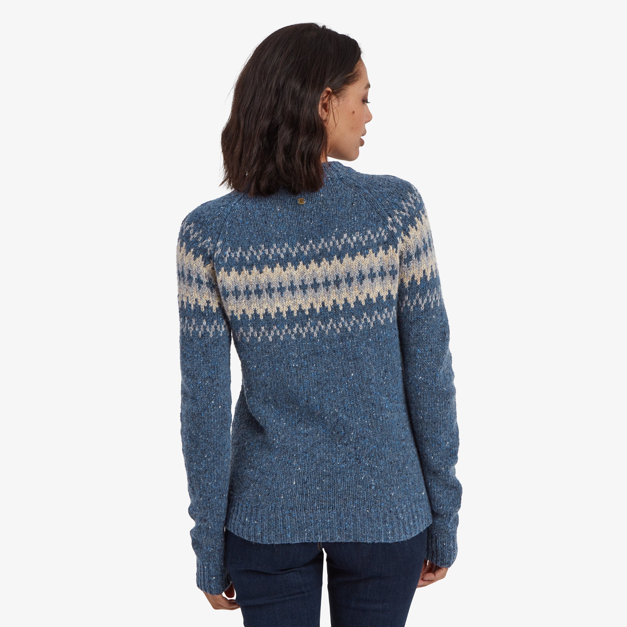 The model turned around, displaying the back of the Sherpa Adventure Gear Dumji Crew Sweater in Blue. The Nordic pattern wraps around the shoulders and upper back, while the lower half is solid blue. The back shot highlights the overall fit and length, which reaches just below the hips.