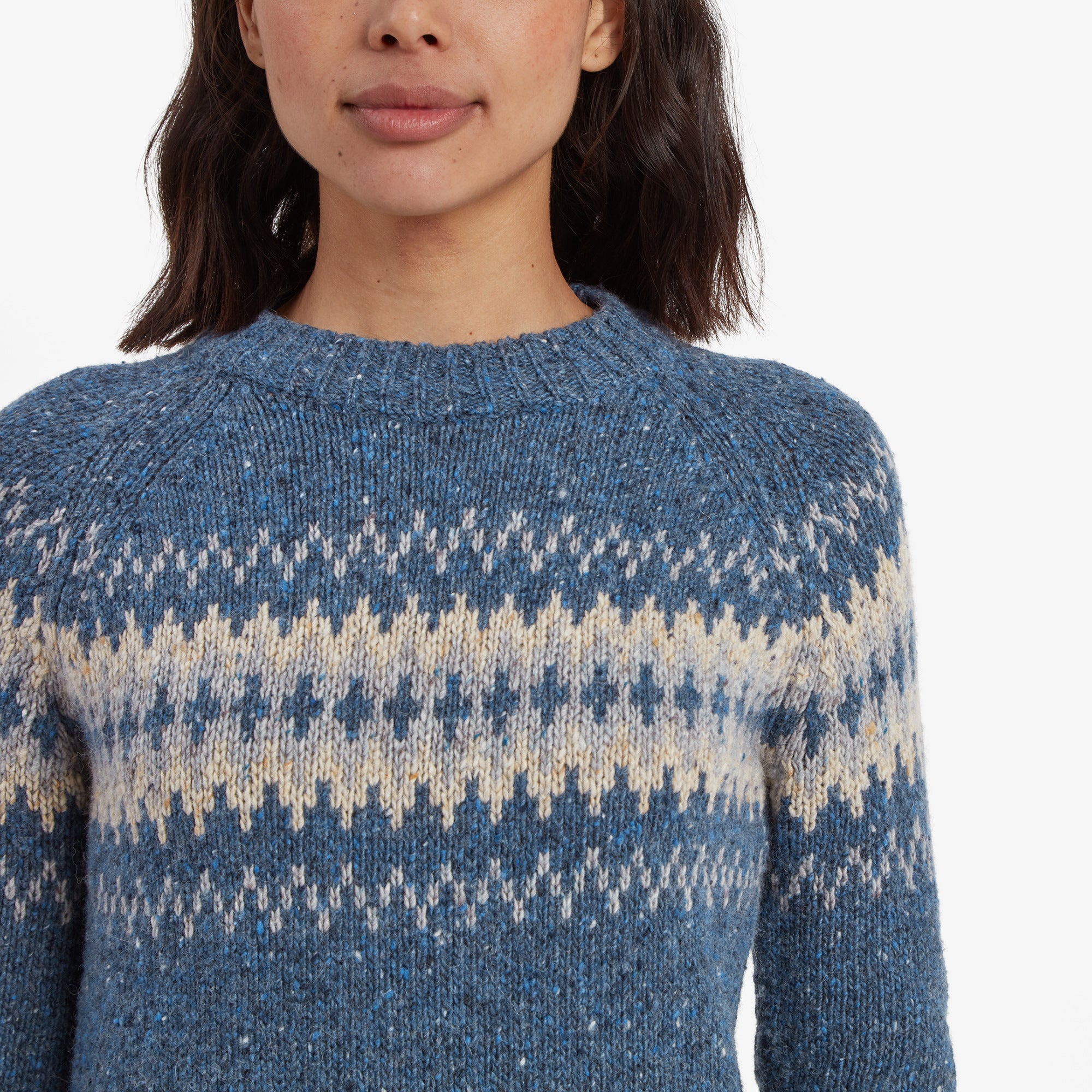 A close-up view of the upper chest area of the Sherpa Adventure Gear Dumji Crew Sweater in Blue, showing the intricate knit details of the beige and light gray Nordic pattern against the blue background. The ribbed neckline is also visible, emphasising the craftsmanship and texture of the garment.