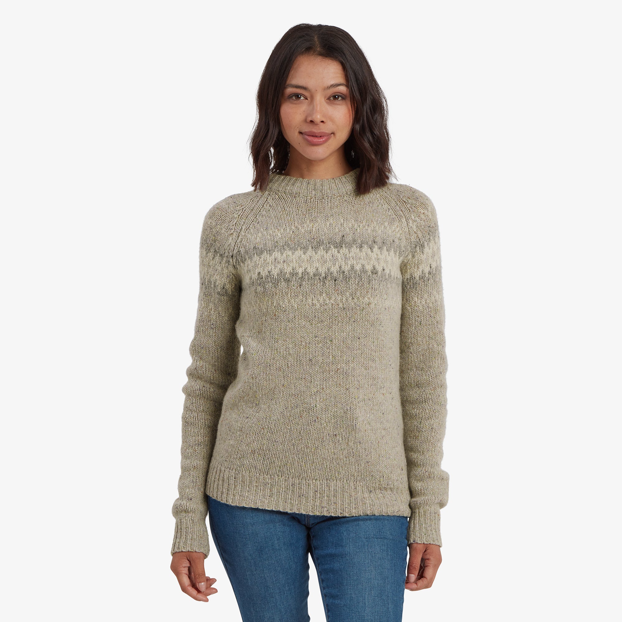 A woman is wearing a Sherpa Adventure Gear Dumji Crew Sweater in Brown with a textured knit design featuring a zigzag pattern across the chest and shoulders. The sweater has ribbed cuffs and hem, and the model pairs it with blue denim jeans. She is standing with a neutral expression, looking directly at the camera.