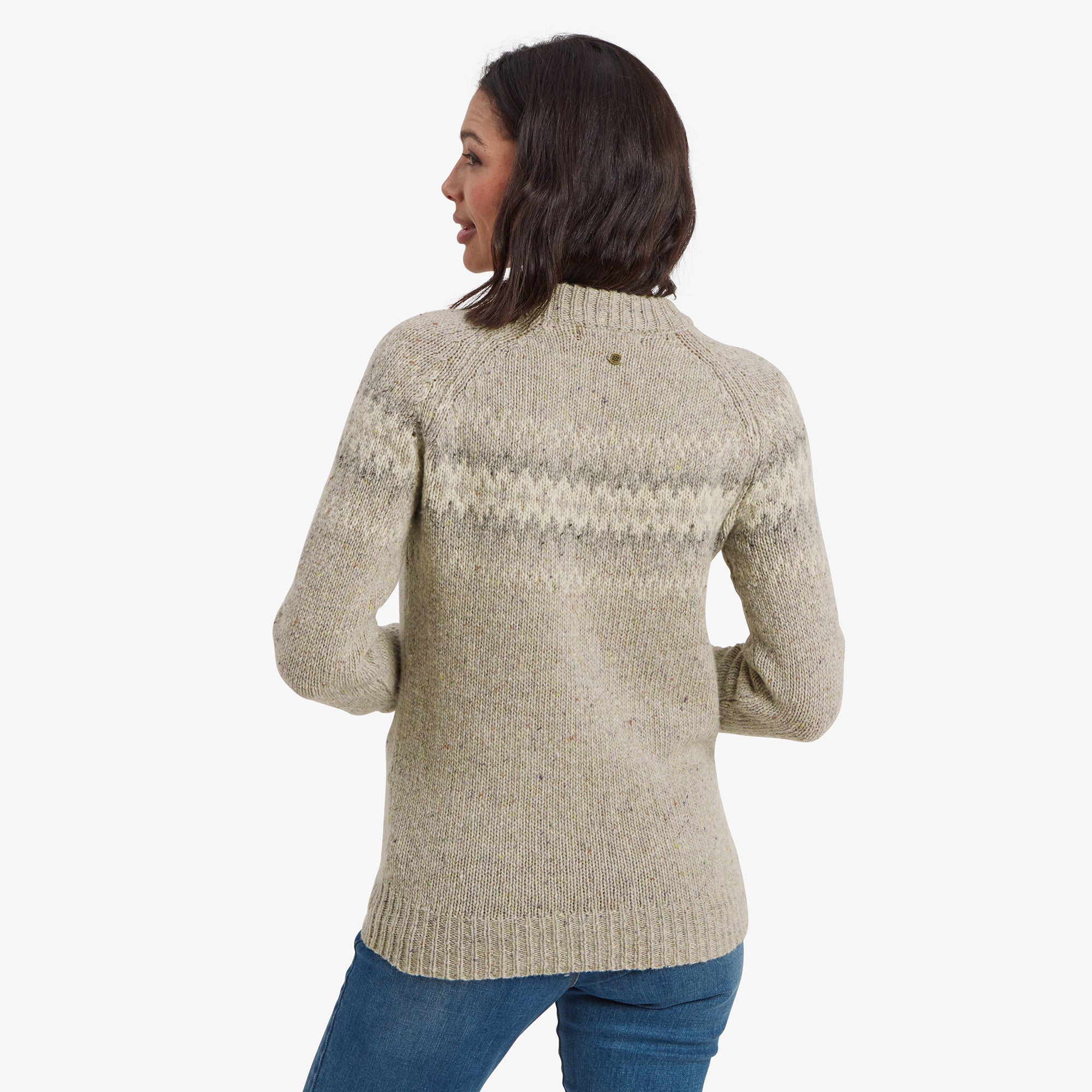 The model is shown from the back, highlighting the back design of the Sherpa Adventure Gear Dumji Crew Sweater in Brown. The zigzag pattern continues seamlessly across the shoulders. Her arms hang naturally at her sides, showcasing the ribbed cuffs and hemline.