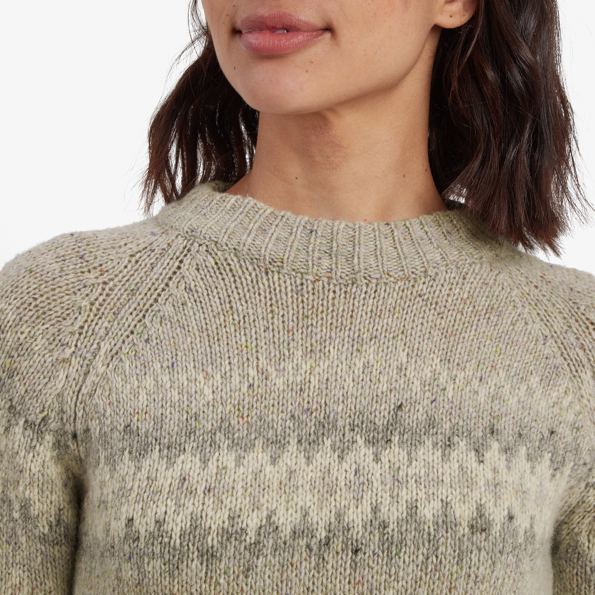 A close-up shot focuses on the textured knit design of the Sherpa Adventure Gear Dumji Crew Sweater in Brown, particularly the intricate zigzag pattern across the chest. The ribbed neckline and fine detailing of the fabric are clearly visible, showcasing the craftsmanship of the knitwear.