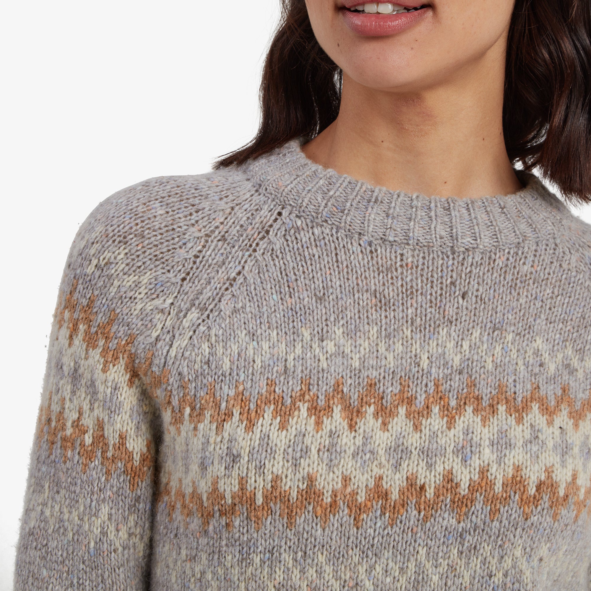 A detailed close-up of the Sherpa Adventure Gear Dumji Crew Sweater in Grey’s upper portion shows the intricate knit pattern and warm color palette of the zigzag design. The ribbed neckline is soft and stretchy, ensuring comfort and style, with the speckled texture adding a modern touch. The texture and craftsmanship of the knit are clearly visible in this shot.