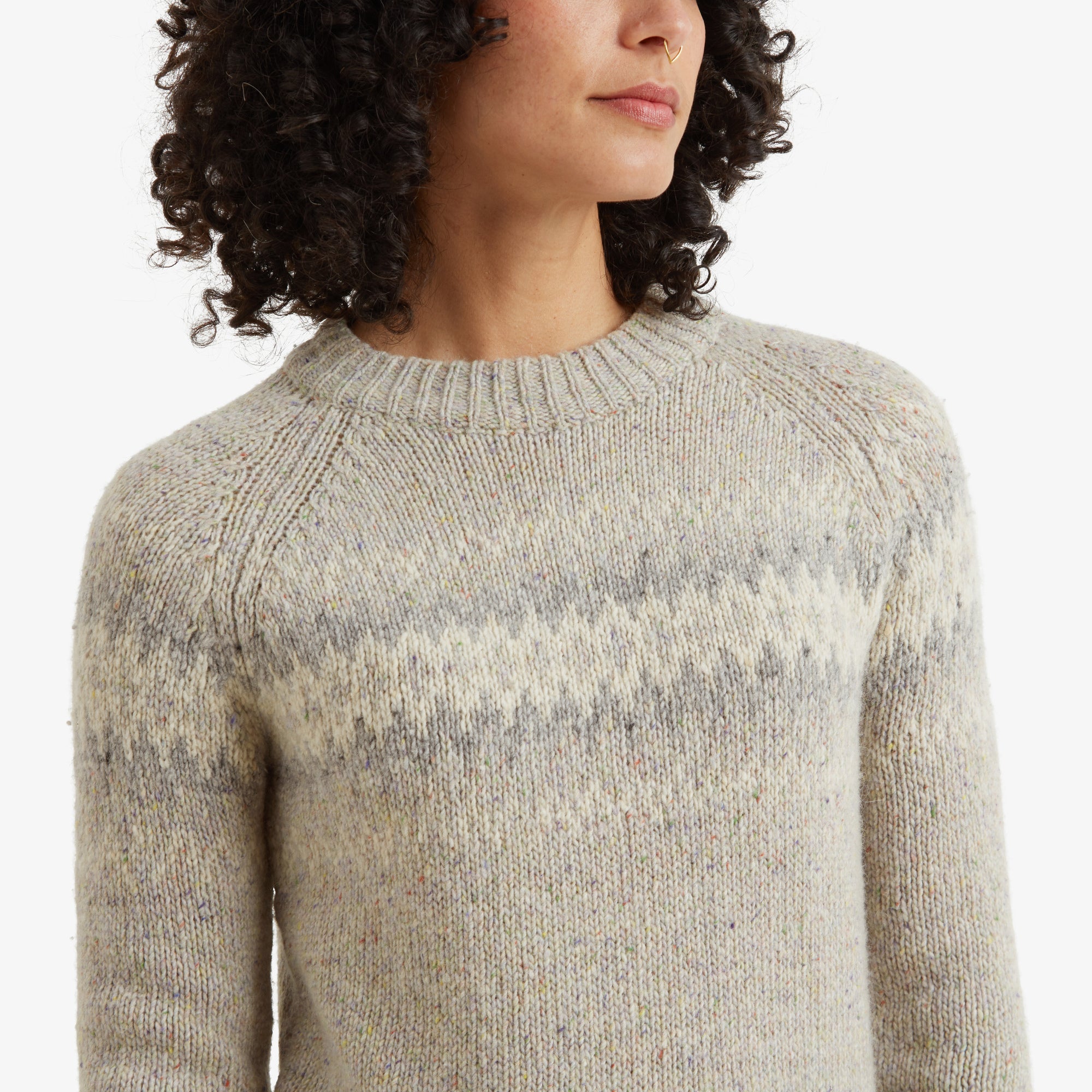 A detailed view of the Sherpa Adventure Gear Dumji Crew Sweater in White’s upper chest and neckline. The crew neck has ribbed detailing, and the geometric pattern in soft gray tones blends harmoniously with the beige base. The knitted texture of the fabric is clearly visible, showcasing its craftsmanship.