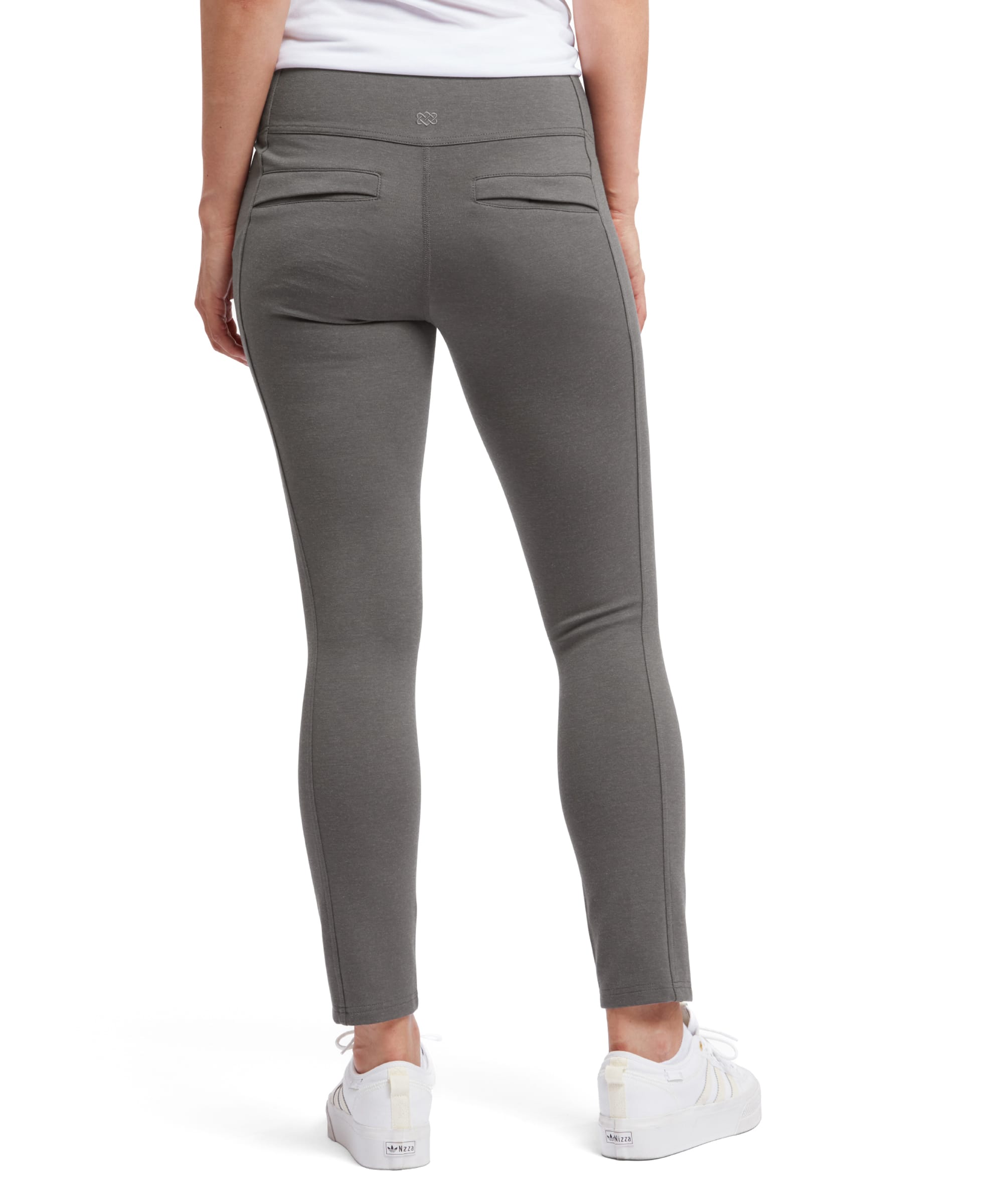 A rear view of the Sherpa Adventure Gear Hapta Knit trousers in Grey, highlighting the back details. The high-rise waistband sits comfortably at the waist, and the trousers feature two back slit pockets with a minimalist design. The stitching is clean and precise, ensuring a tailored finish. The slim, straight-leg fit elongates the legs and ends neatly at the ankle. The model's white trainers add contrast to the neutral grey color of the trousers.