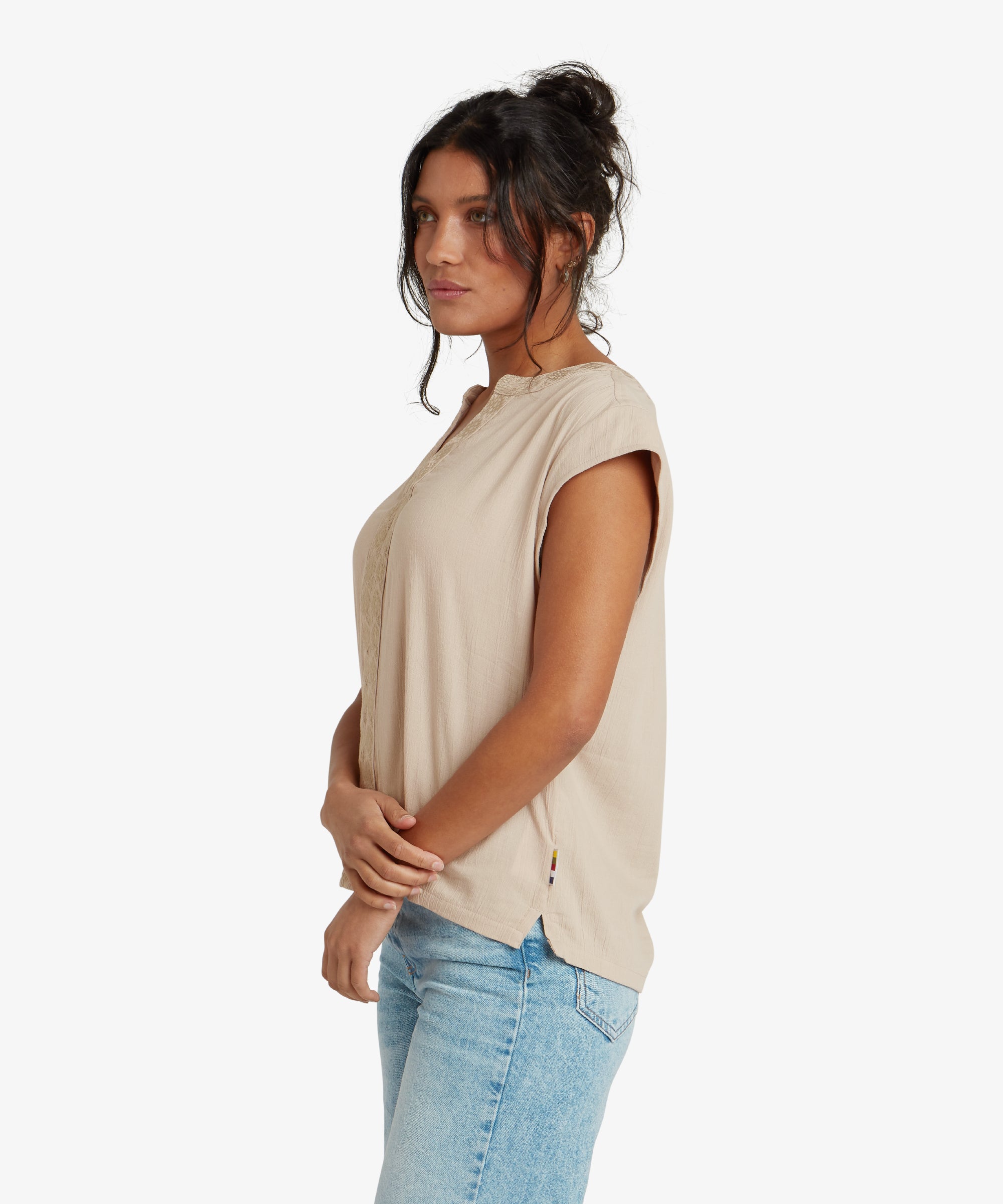 A back view of the Sherpa Adventure Gear Hara Cap Sleeve Top in Beige. The shirt has soft gathers at the back neckline, creating a flattering silhouette. A small decorative button detail is visible at the center-back neckline, complementing the minimalist design.