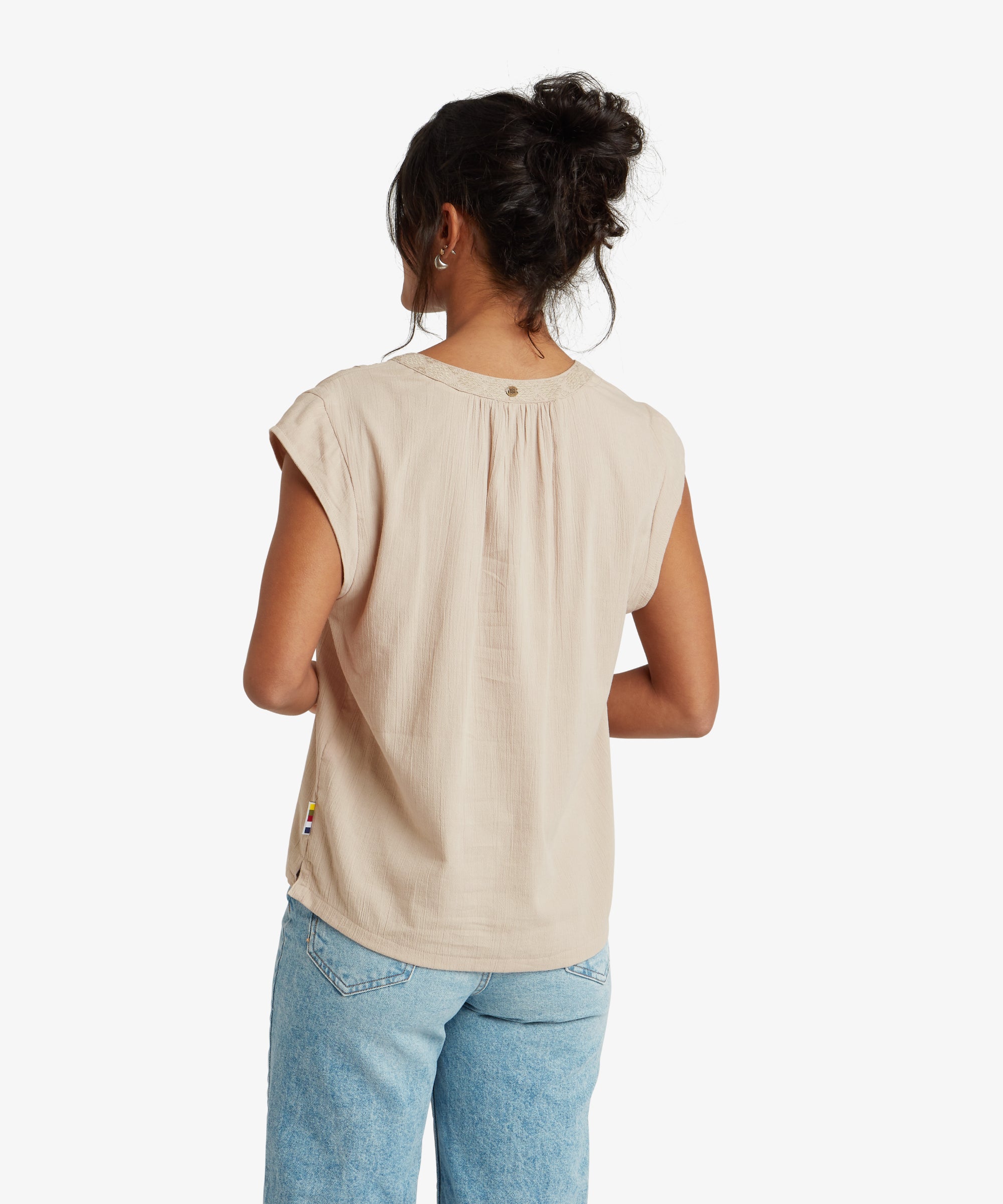 A close-up of the Sherpa Adventure Gear Hara Cap Sleeve Top in Beige's neckline and embroidery. The intricate vertical embroidered detail stands out against the lightweight fabric. The woman wears a delicate gold necklace that adds an elegant touch to the look.