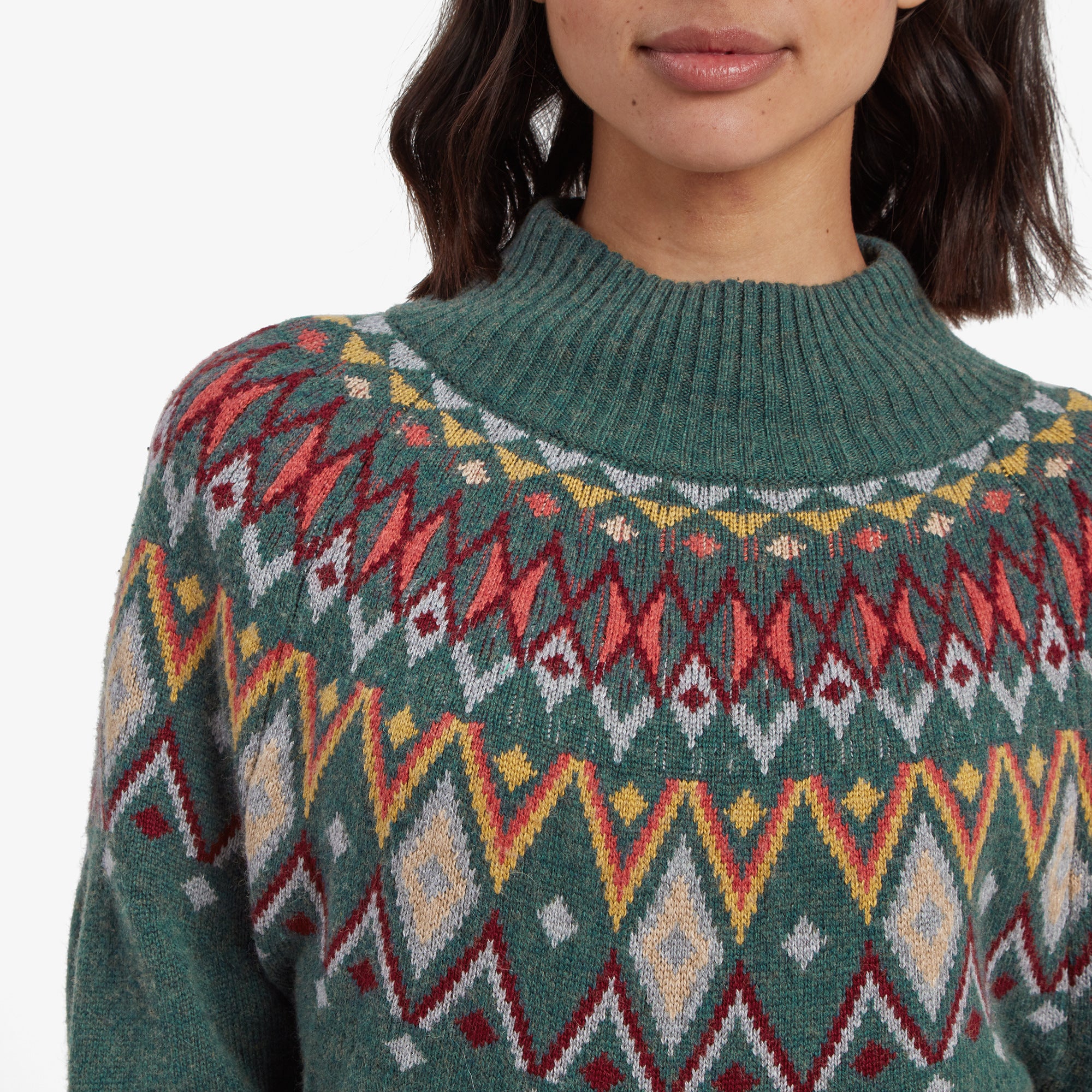 A detailed look at the vibrant Fair Isle knit design on the Sherpa Adventure Gear Indu Eco Mock Neck in Green, showcasing intricate diamond and zigzag patterns in red, yellow, and gray, along with the ribbed mock neckline.