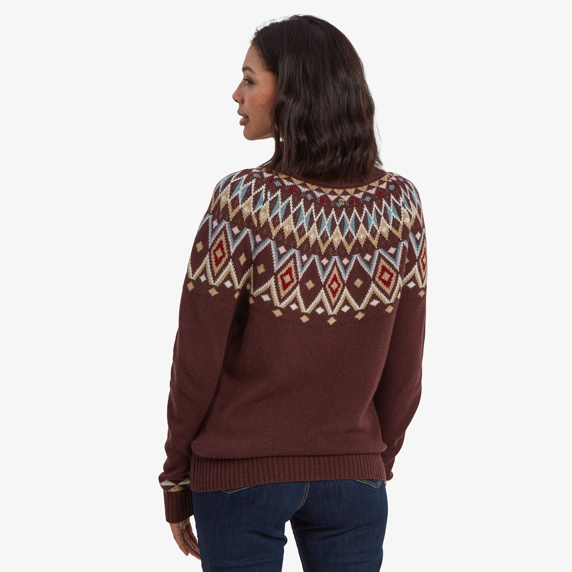 A back view of the Sherpa Adventure Gear Indu Eco Mock Neck Sweater in Red, revealing the continuation of the diamond-patterned yoke around the shoulders. The rest of the sweater is a solid burgundy color, and the hem is ribbed. The model's hair is styled in soft waves.