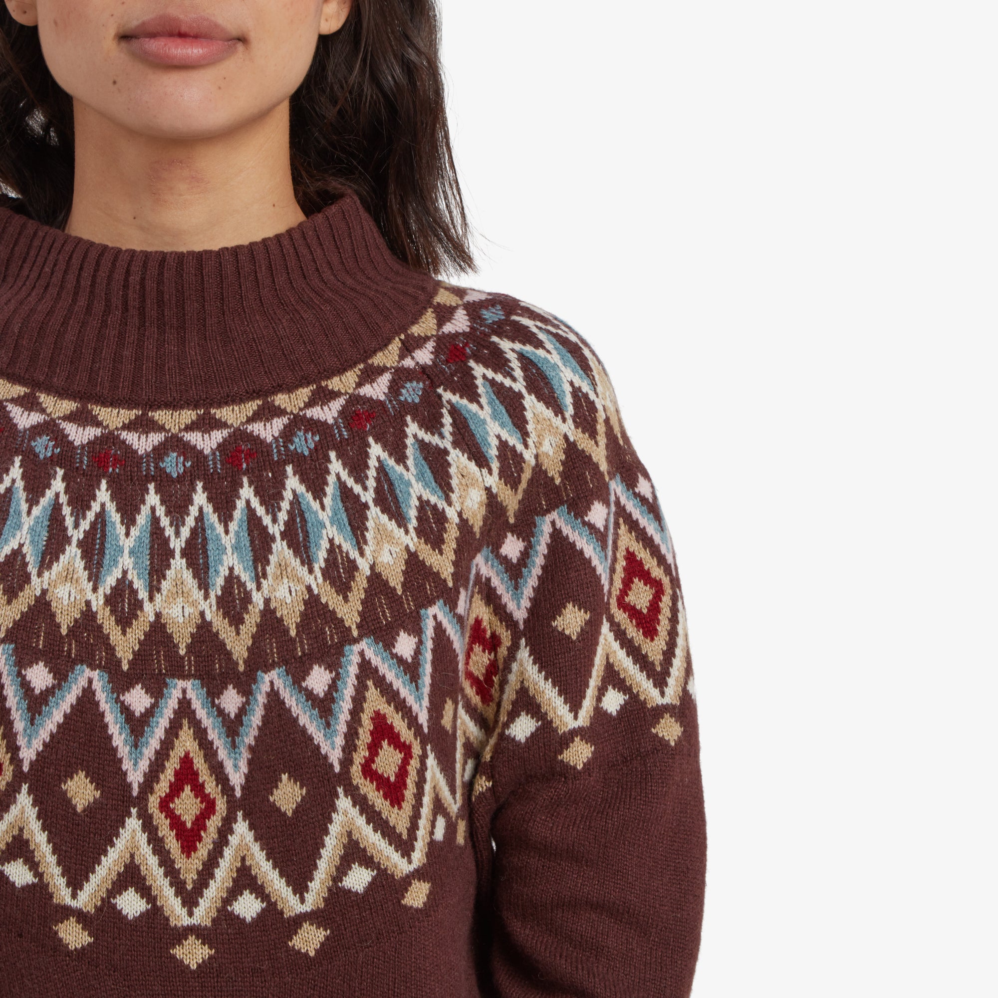 A close-up of the Sherpa Adventure Gear Indu Eco Mock Neck Sweater in Red's upper portion, focusing on the diamond pattern. The knit detailing and color contrasts between burgundy, cream, blue, and red are clearly visible, highlighting the craftsmanship.