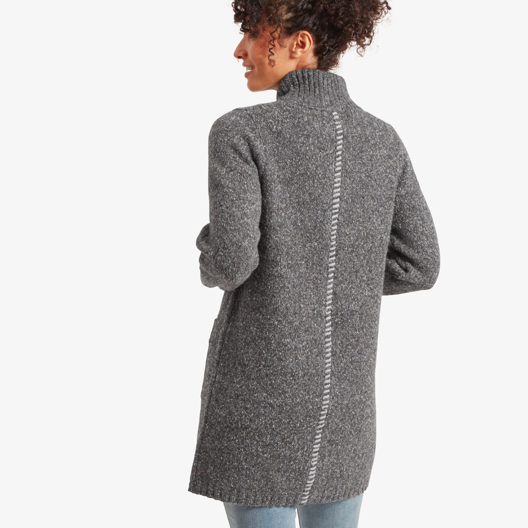 Back view of the same Sherpa Adventure Gear Jaga Full Zip Duster in Grey, showcasing a unique knitted seam detail running down the center. The ribbed high collar and the longline length of the cardigan add elegance, paired with light blue jeans.