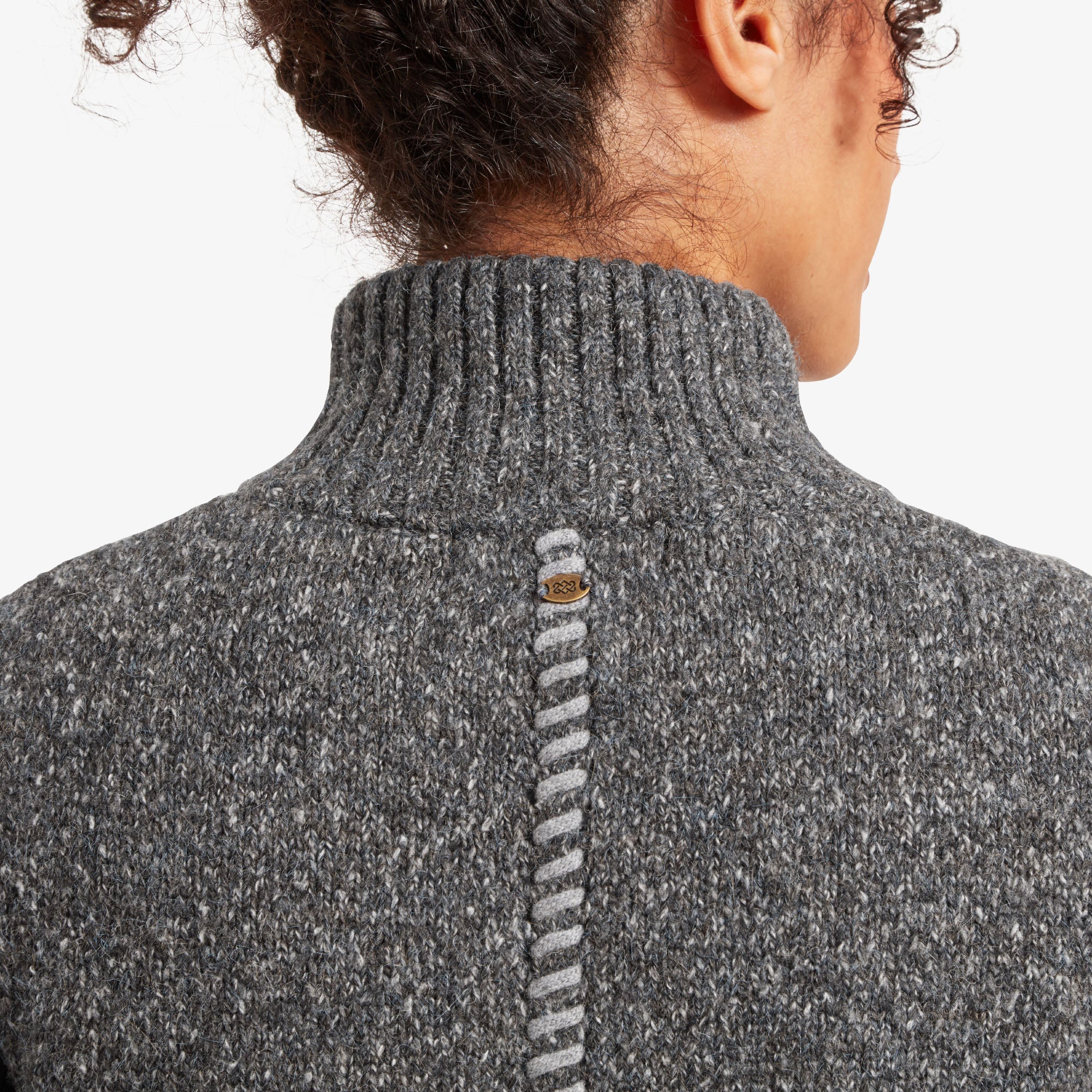 A close-up of the back neckline, showing the detailed knitwork and a decorative logo tag at the center. The ribbed high collar seamlessly transitions into the unique central back seam, adding a touch of craftsmanship to the Sherpa Adventure Gear Jaga Full Zip Duster in Grey's design.