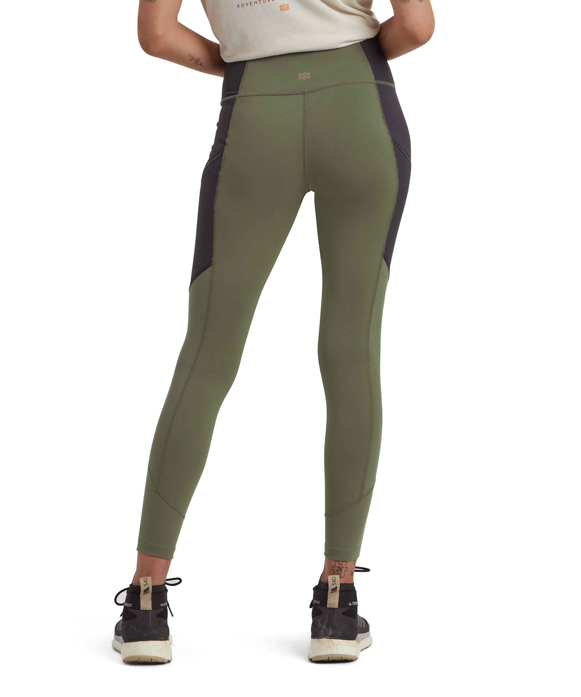 The rear view of Sherpa Adventure Gear Kalpana Tight in Green with black side panels, highlighting the waistband and seam details for a flattering fit. The Sherpa logo is subtly placed on the waistband. The model pairs the leggings with black trail trainers and a light t-shirt.