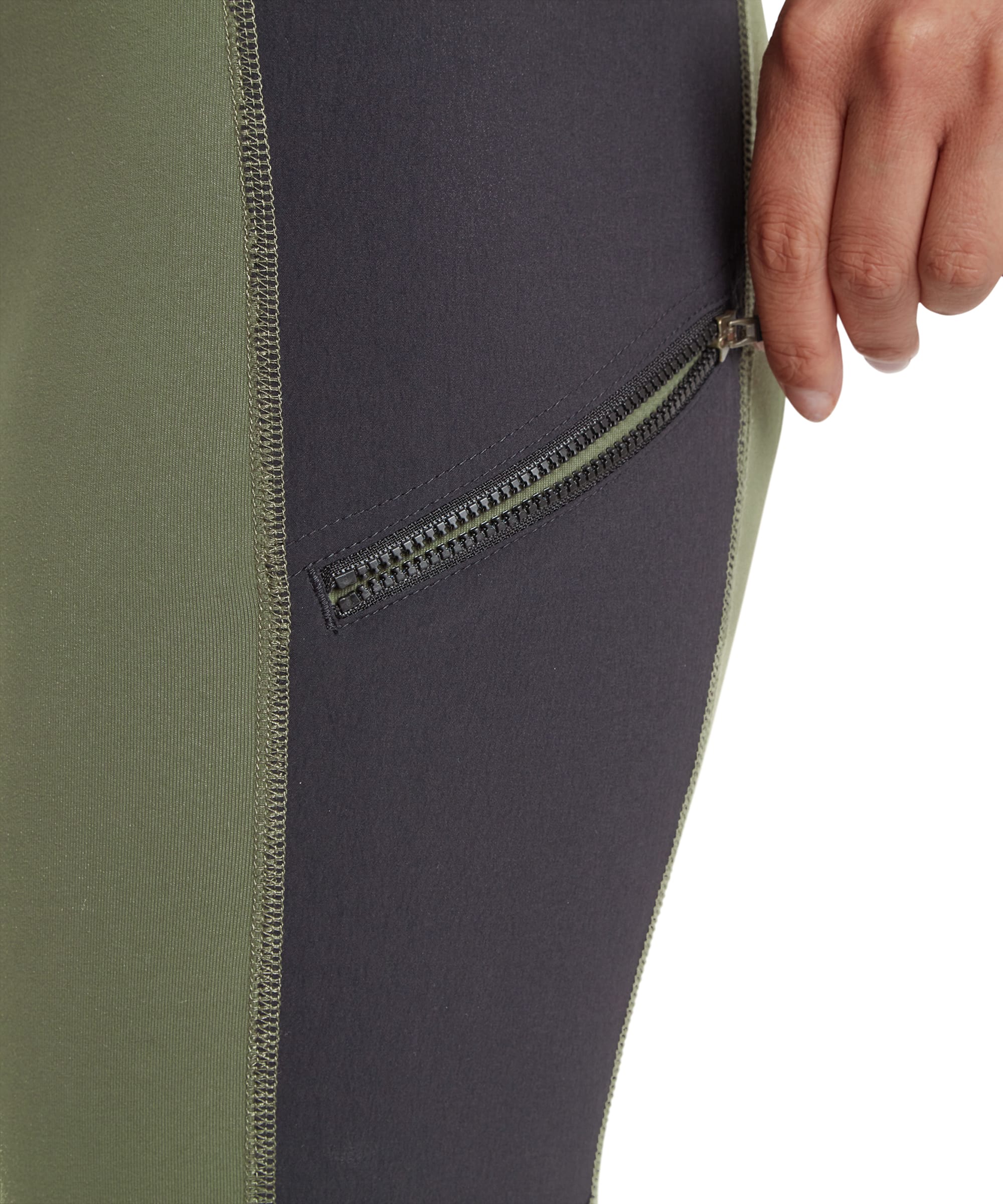 A close-up shot of the black side pocket on the Sherpa Adventure Gear Kalpana Tight in Green, showcasing a secure zipper. The pocket is integrated into the black contrast panel, providing a functional feature for small essentials.