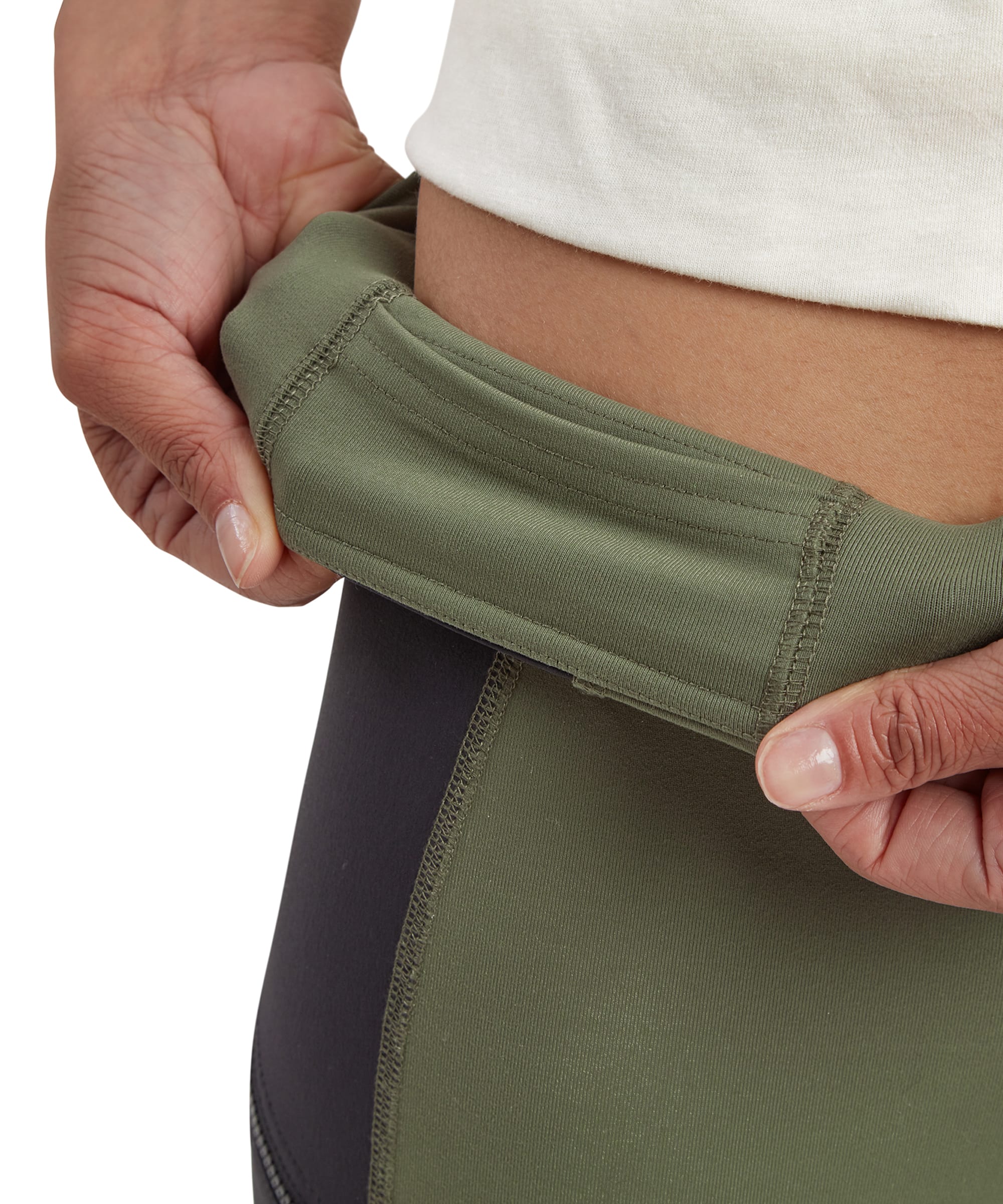 A close-up image of the waistband of the Sherpa Adventure Gear Kalpana Tight in Green being gently stretched by the model. The waistband features a soft, supportive design, emphasising its comfort and adjustability for various activities.