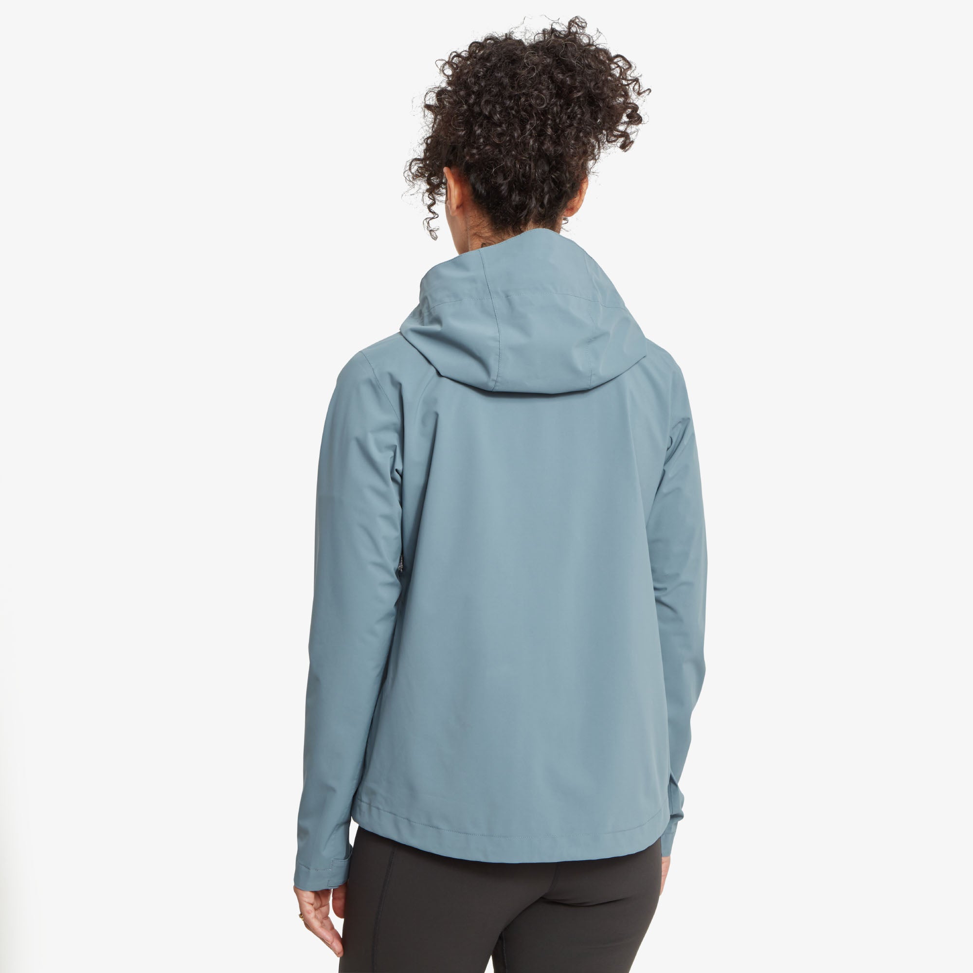 A rear view showcasing the Sherpa Adventure Gear Nima 2.5-Layer Jacket in Blue's streamlined design. The hood is visible, resting flat against the back. The clean cut extends to a slightly curved hemline, emphasising the lightweight material and functional design.