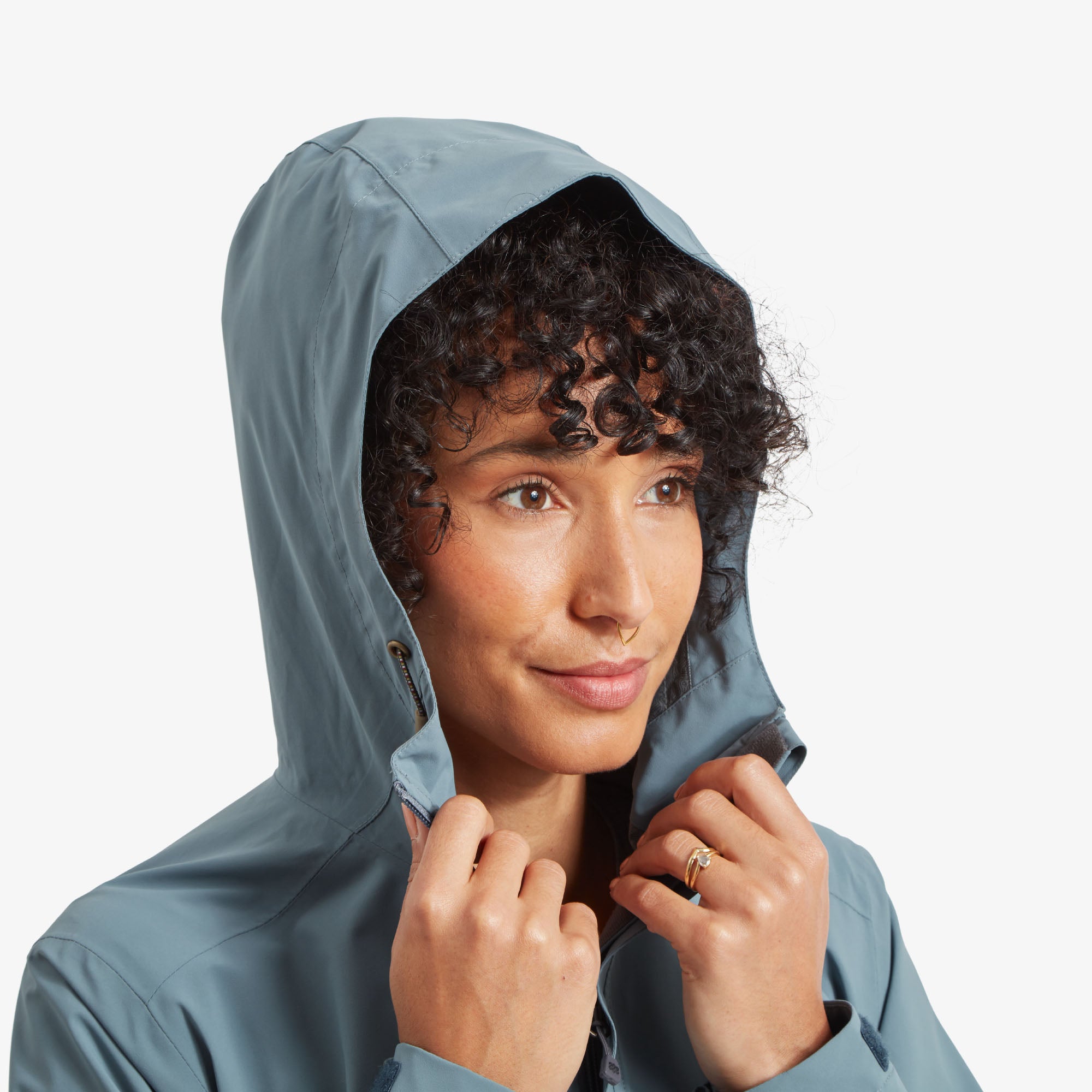 A close-up of the model adjusting the hood of the Sherpa Adventure Gear Nima 2.5-Layer Jacket in Blue, highlighting the textured drawstrings with toggle stoppers for adjustability. The hood's seamless integration with the jacket provides full coverage, suitable for wet or windy weather.