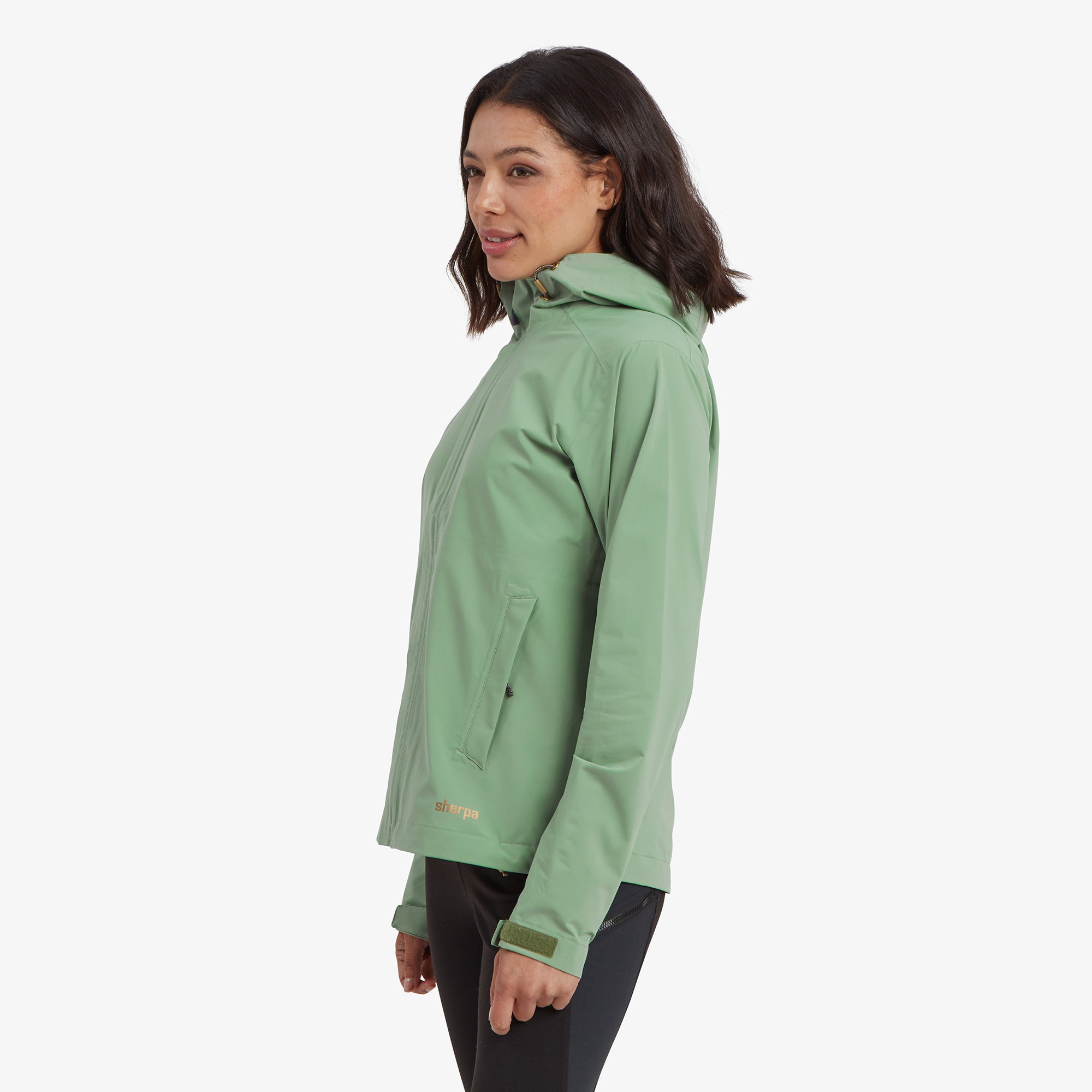 A profile shot of the model wearing the Sherpa Adventure Gear Nima 2.5-Layer Jacket in Green, showing the side seam, zippered pockets, and articulated sleeves for movement.