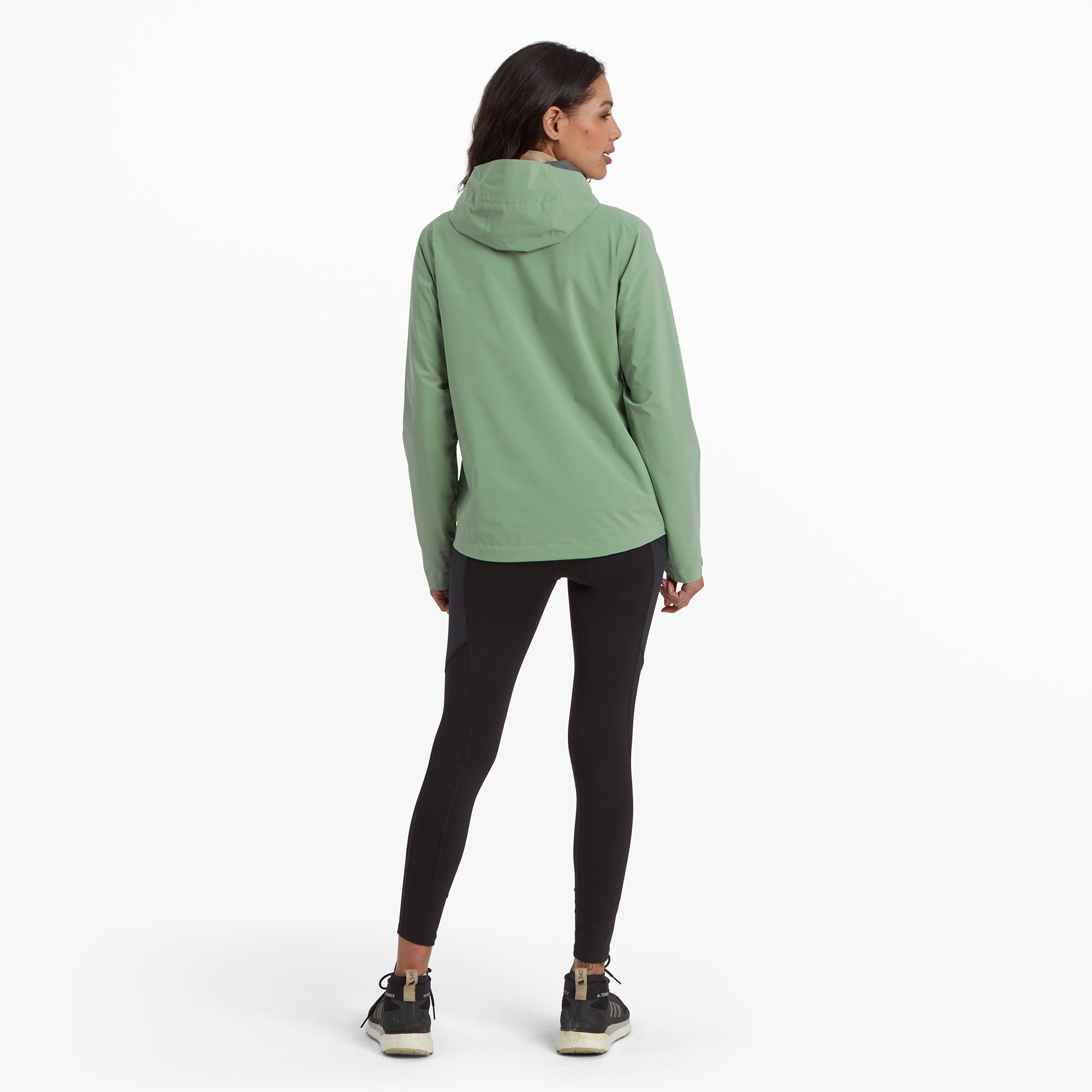 The model is seen from behind, showcasing the hood's structure and the clean, simple back design of the Sherpa Adventure Gear Nima 2.5-Layer Jacket in Green.