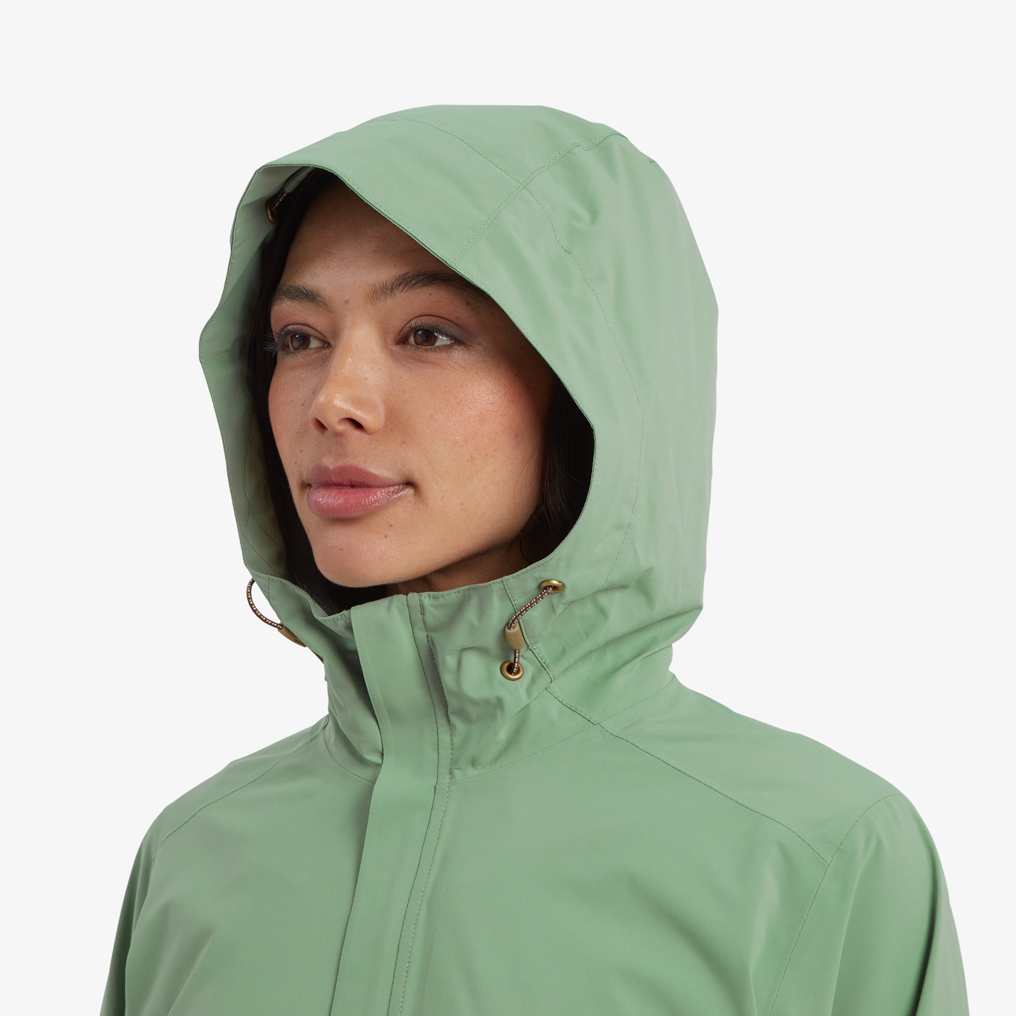 A detailed shot of the model's face with the hood up on the Sherpa Adventure Gear Nima 2.5-Layer Jacket in Green, emphasising the soft fabric, gold hardware, and drawstring details.