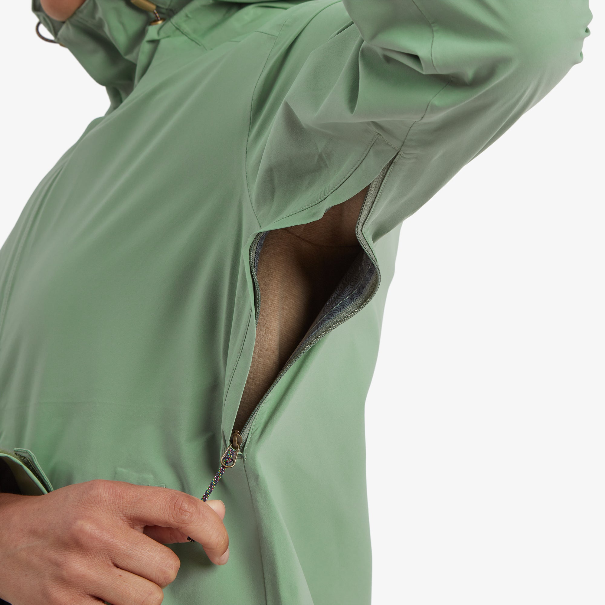 A close-up of the model demonstrating the zippered underarm ventilation for breathability, revealing a light lining inside on the Sherpa Adventure Gear Nima 2.5-Layer Jacket in Green.