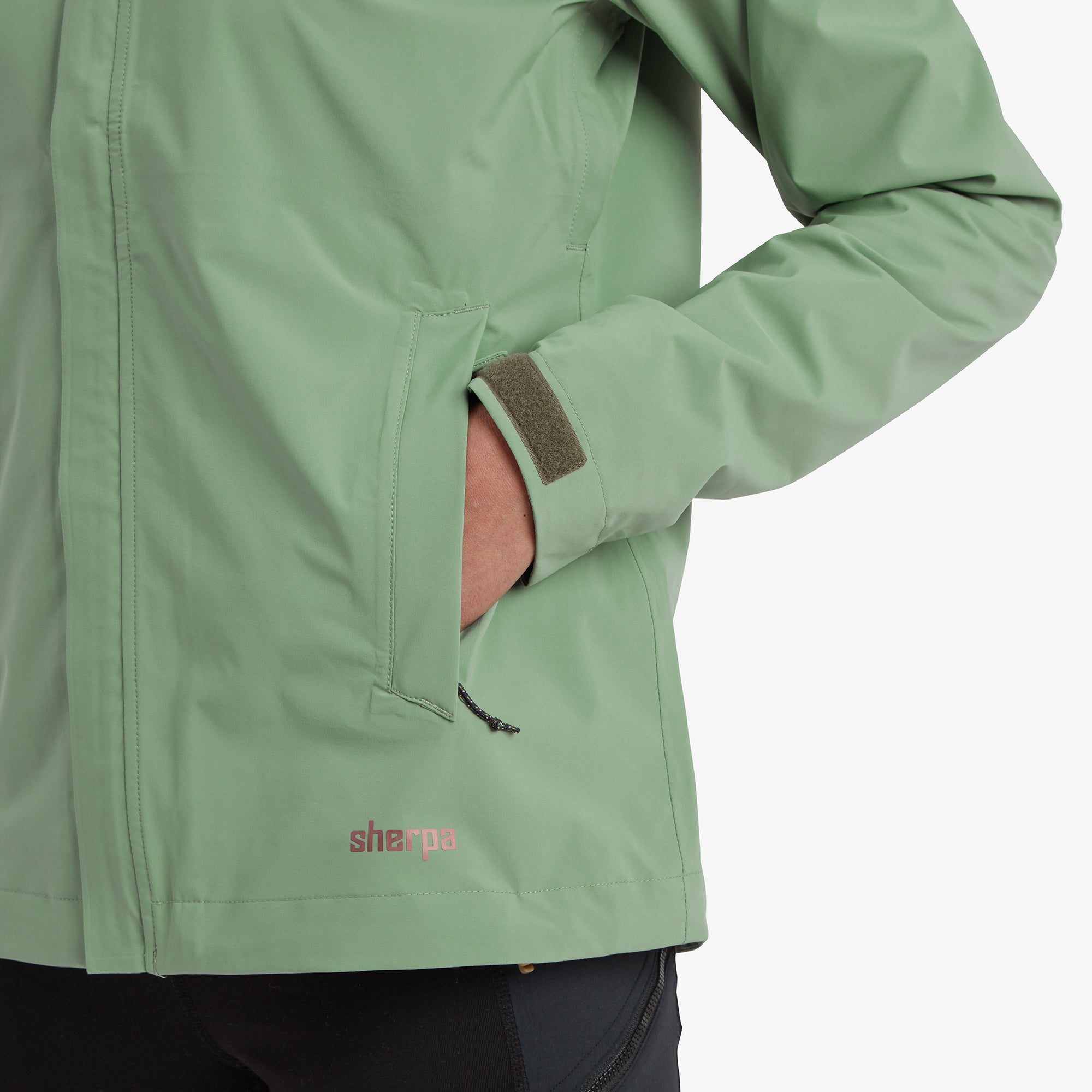 A focused image of the jacket’s zippered front pocket, with the Sherpa logo subtly embossed near the hem.