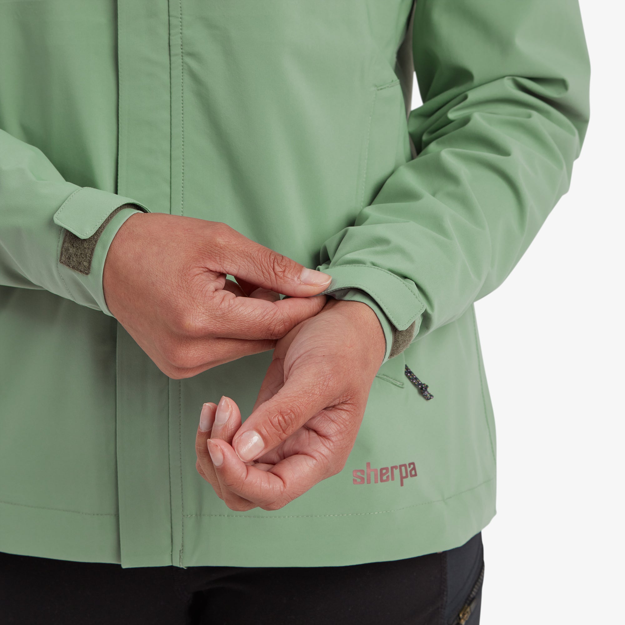 A close-up of the model's hands adjusting the Velcro wrist cuffs, showing the functionality and fit customization of the sleeves on the jacket.