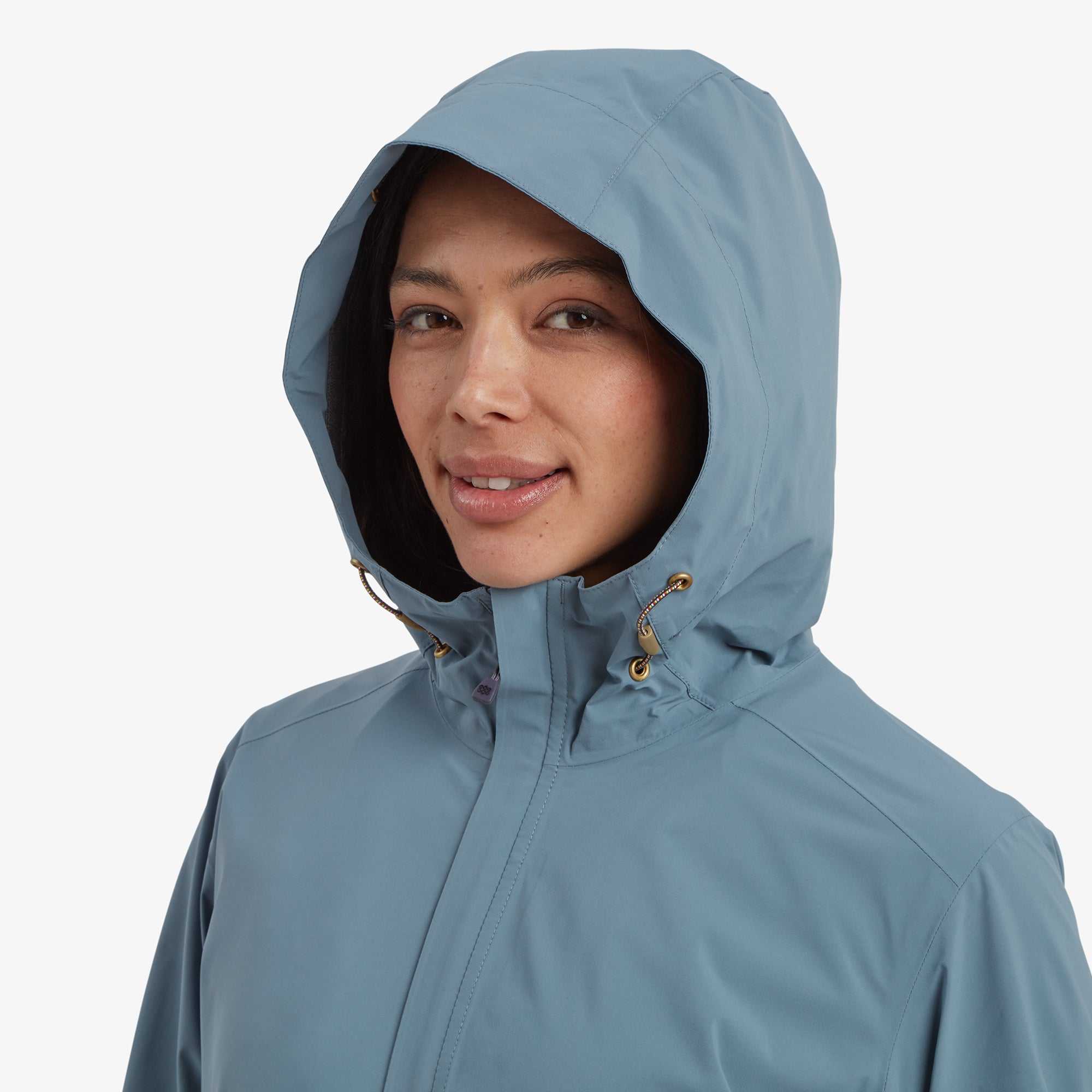 A close-up of the woman's face with the hood up on the Sherpa Adventure Gear Nima 2.5-Layer Long Jacket in Blue, highlighting the secure fit of the hood with its adjustable drawstrings, ideal for protecting against the elements.