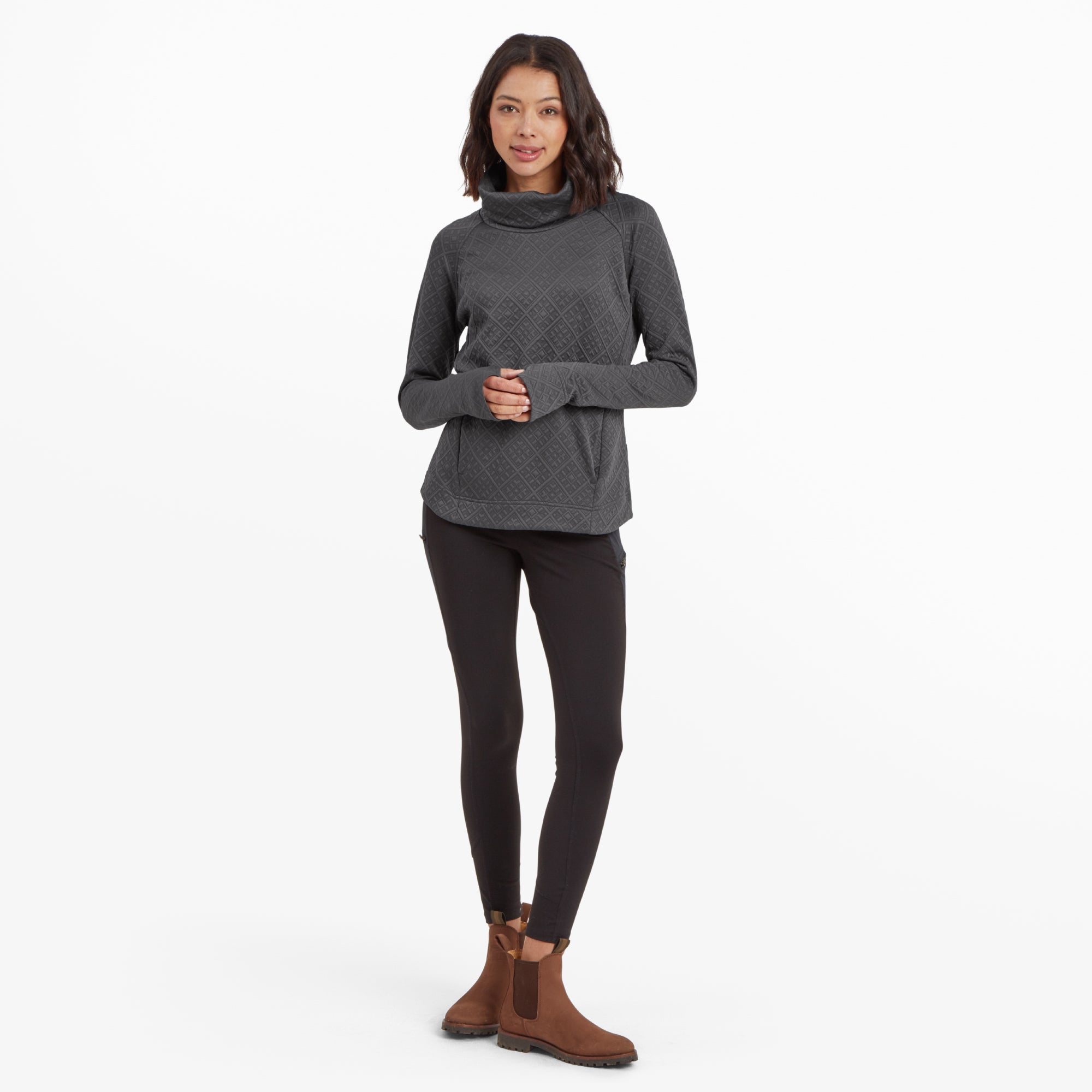 The same model is shown in a full-body shot, wearing the Sherpa Adventure Gear Nyano Pullover in Grey along with black leggings and brown ankle boots. Her hands are clasped in front of her, highlighting the pullover's relaxed fit, long sleeves, and slightly curved hem.