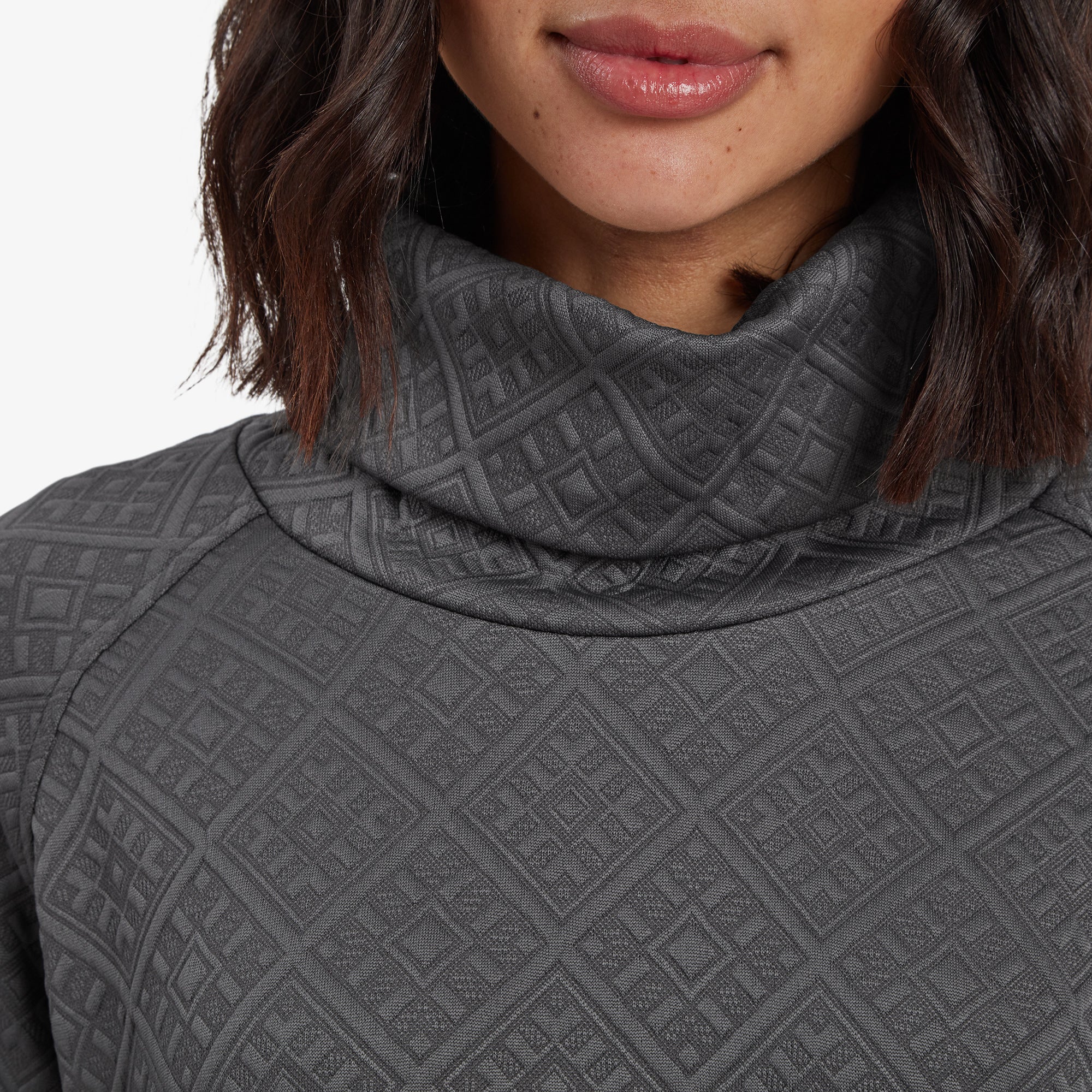 A close-up view focusing on the Sherpa Adventure Gear Nyano Pullover in Grey’s cowl neck. The soft draped neckline features the same grey diamond pattern, showing the texture in detail. The edge of the pullover’s shoulder seam is also visible.