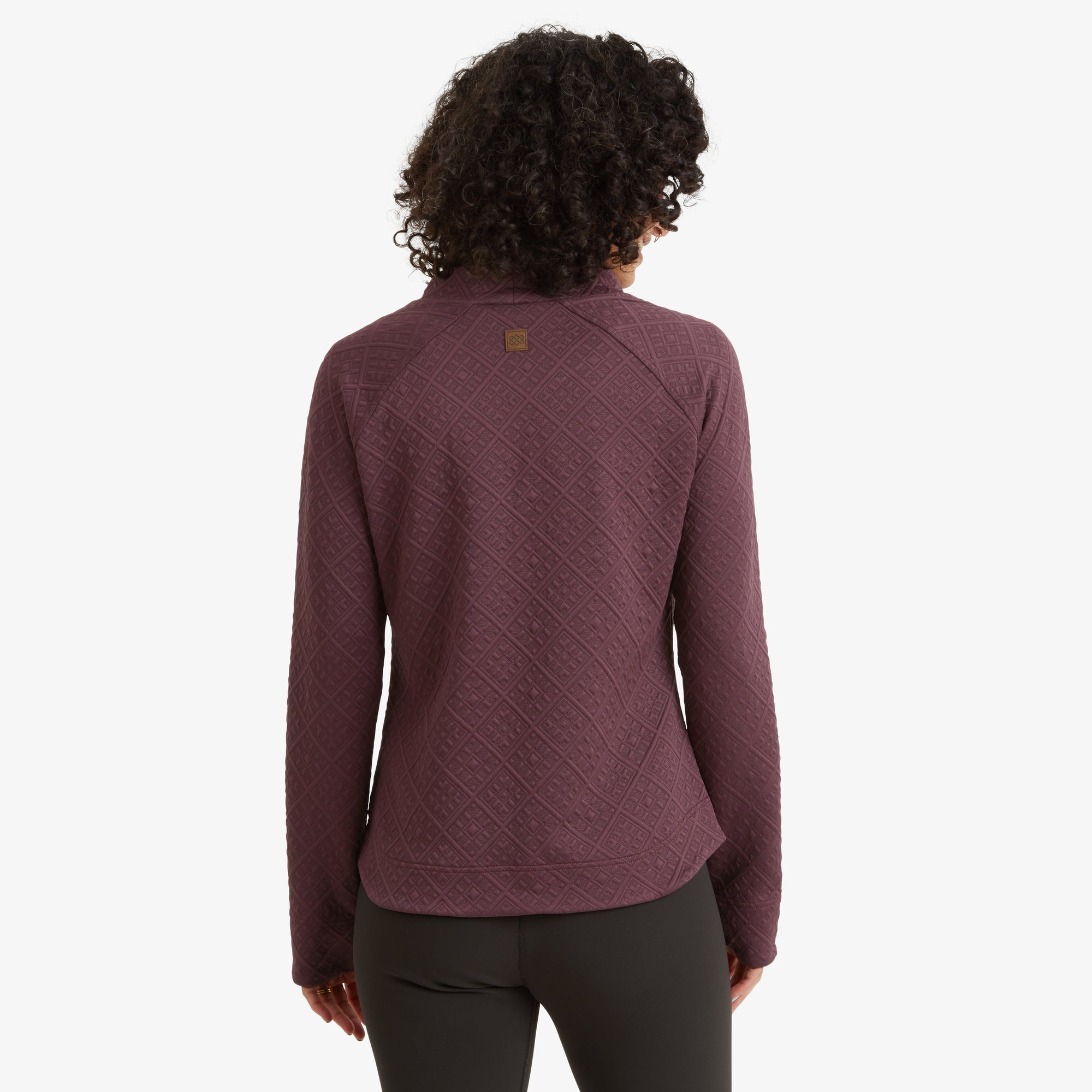 The model is seen from the back, displaying the detailed geometric pattern on the fabric. The Sherpa Adventure Gear Nyano Pullover in Purple has a slightly curved hem and a small brand logo near the upper back.