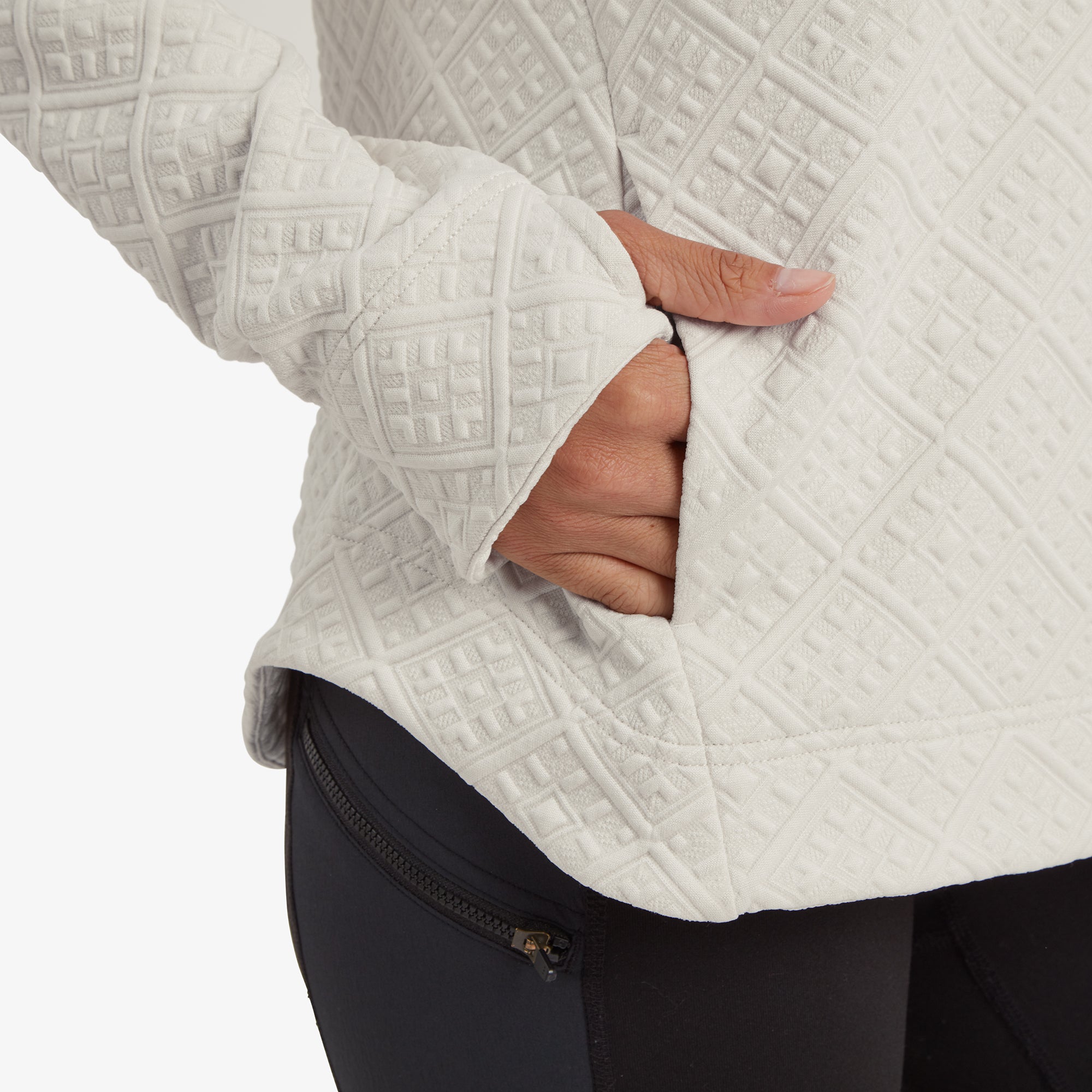 A detailed view of the Sherpa Adventure Gear Nyano Pullover in White’s side pocket. The hand-warmer pocket blends seamlessly into the quilted fabric, with thumbhole details on the sleeves visible, emphasising the pullover's practical and cozy design. The pairing with black leggings highlights its casual, everyday versatility.