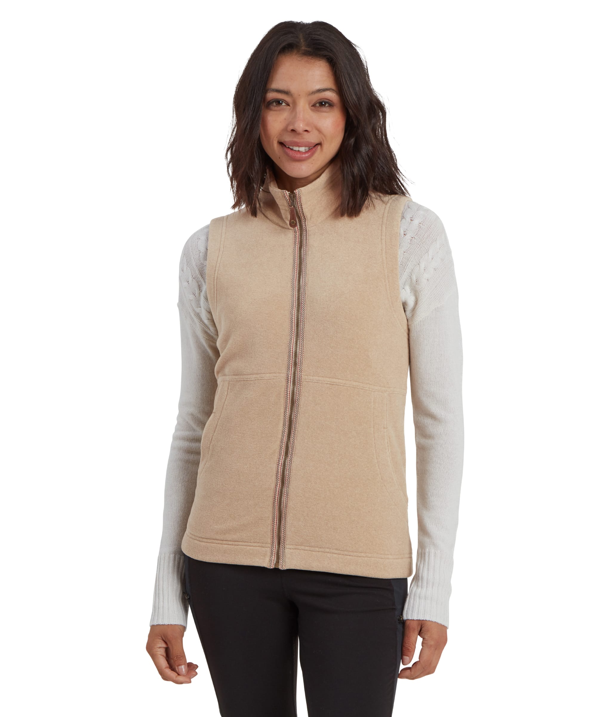 A woman wearing a Sherpa Adventure Gear Rolpa Eco Vest in Beige with a zippered front, layered over a white sweater with textured knit sleeves. She is posing confidently with a subtle smile. The gilet features a clean, minimalistic design with visible seam detailing, creating a sleek and functional look.