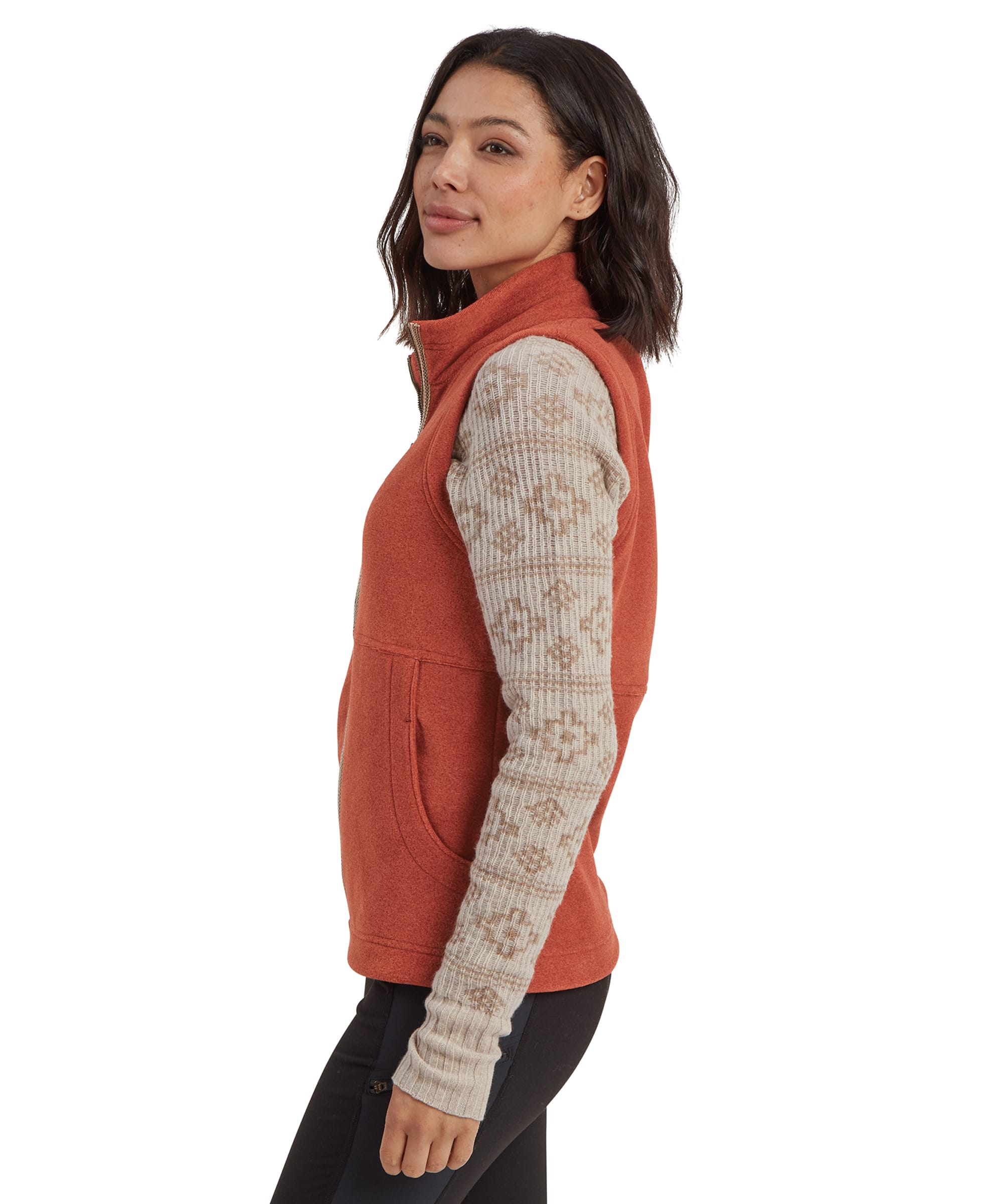 A side profile of the woman wearing the Sherpa Adventure Gear Rolpa Eco Vest in Brown, focusing on the fit and tailored cut along the side. The combination of the rust color and beige-patterned sleeve adds a stylish contrast to the outfit.