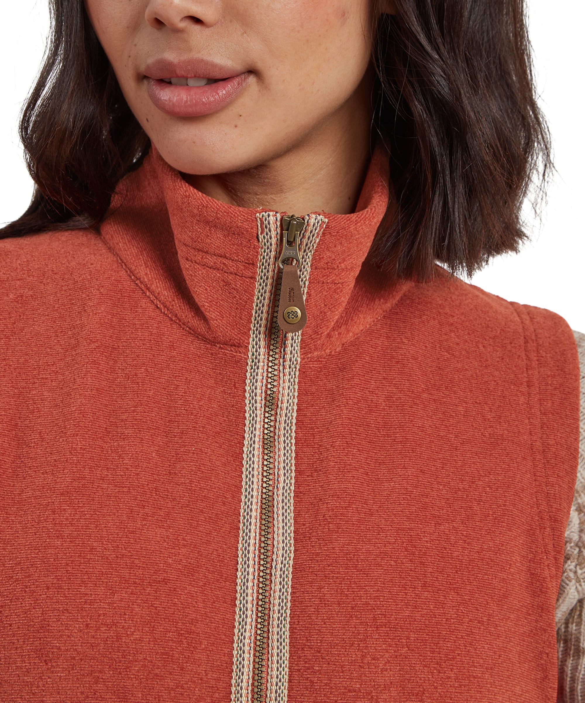 A close-up shot of the Sherpa Adventure Gear Rolpa Eco Vest in Brown's pocket detail, highlighting the pocket's seamless integration into the design. The textured rust fabric contrasts beautifully with the beige sleeve.