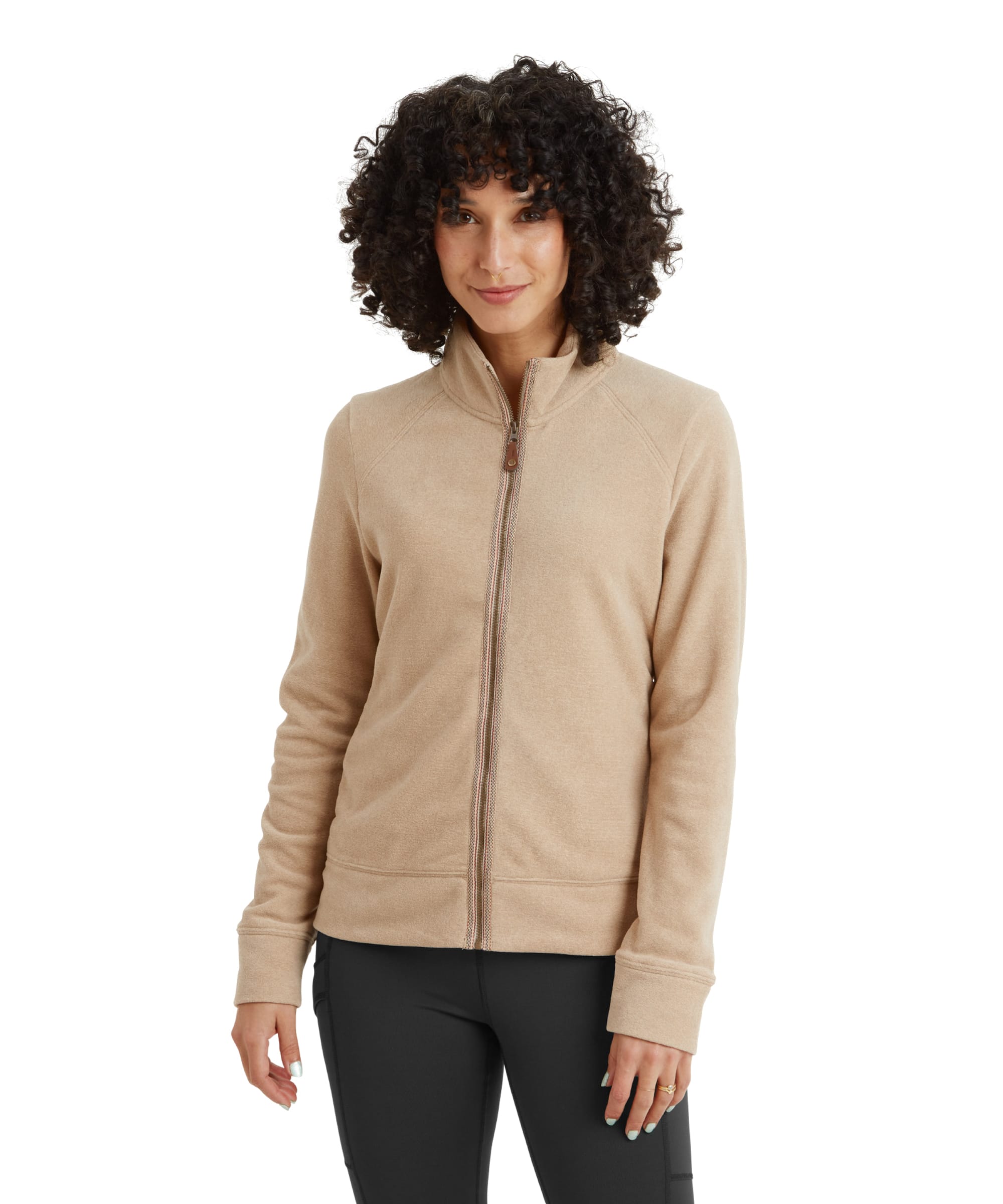 A front-facing view of a woman wearing a Sherpa Adventure Gear Rolpa Eco Jacket in Beige. The jacket features a high collar, full-zip design, and a simple yet cozy fleece texture. She pairs it with black leggings, her hands resting naturally by her sides, exuding a casual and relaxed style.