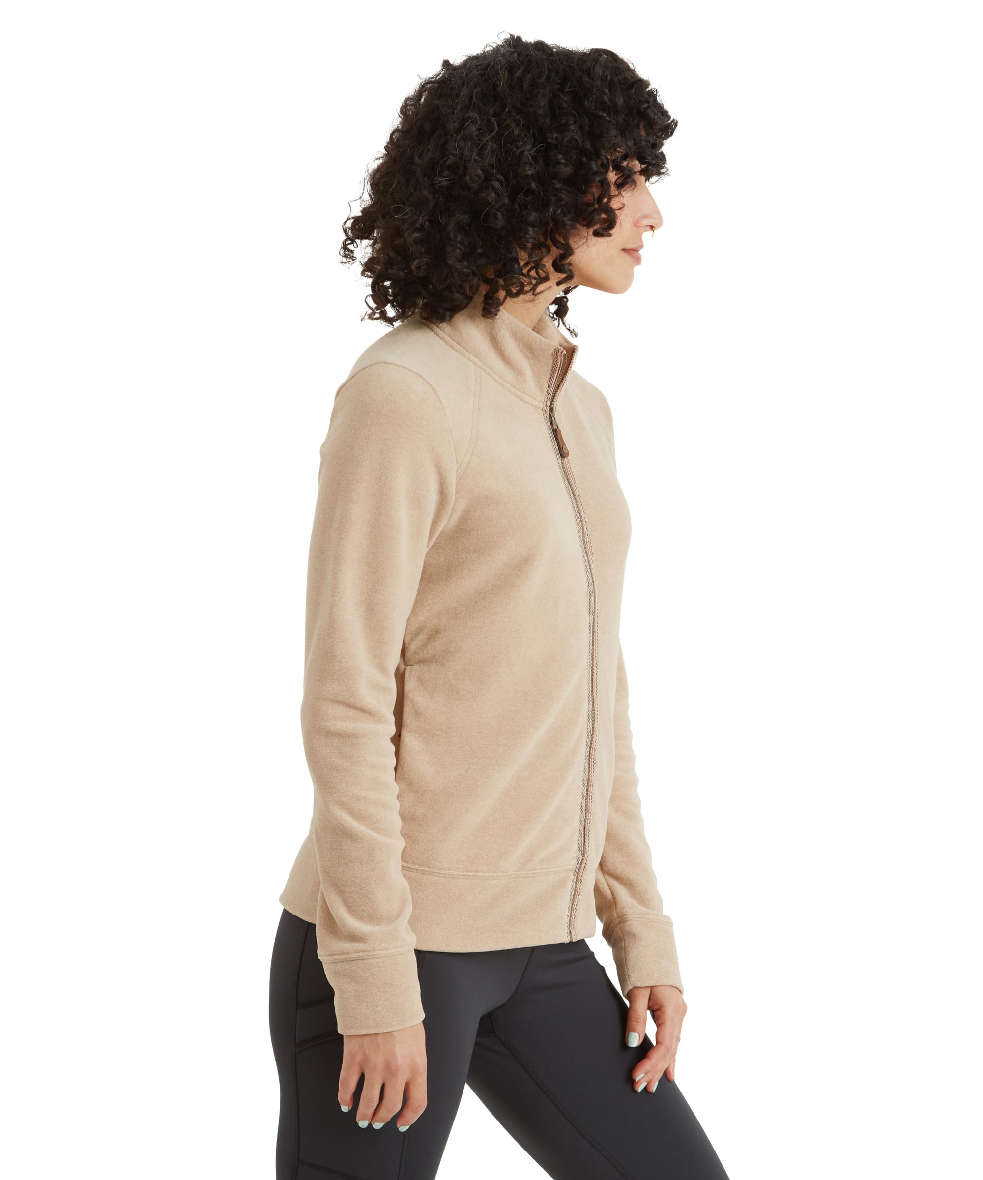 A profile view of the woman wearing the Sherpa Adventure Gear Rolpa Eco Jacket in Beige, highlighting its tailored fit and sleek design. The high collar and full-zip are visible from the side, along with the slight curve of the hem that complements her silhouette.