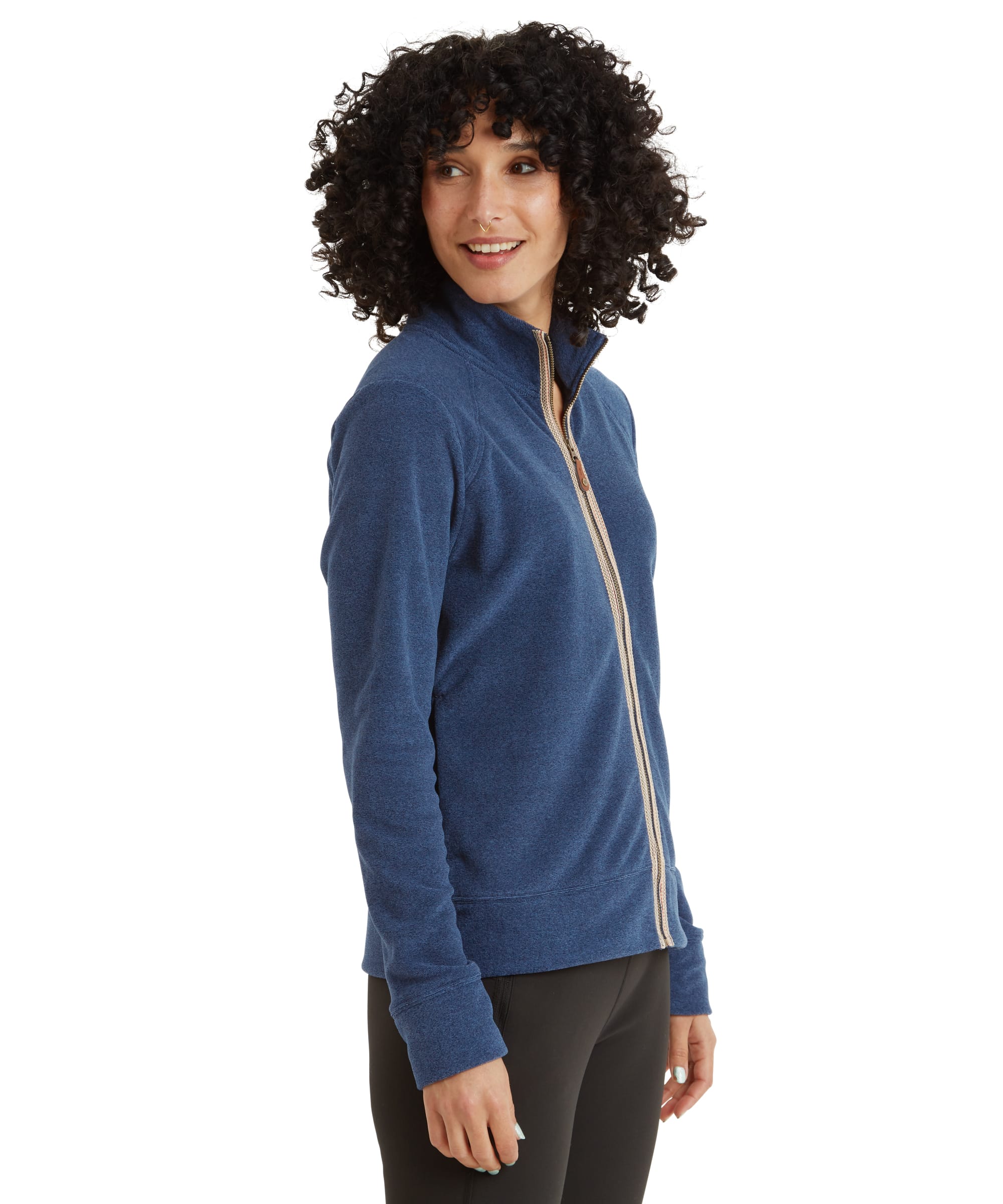 A side profile of the model showcases the Sherpa Adventure Gear Rolpa Eco Jacket in Blue’s tailored fit. The zipper trim is visible, and she is smiling slightly while looking to her right. The sleeves extend just past her wrists with fitted cuffs.