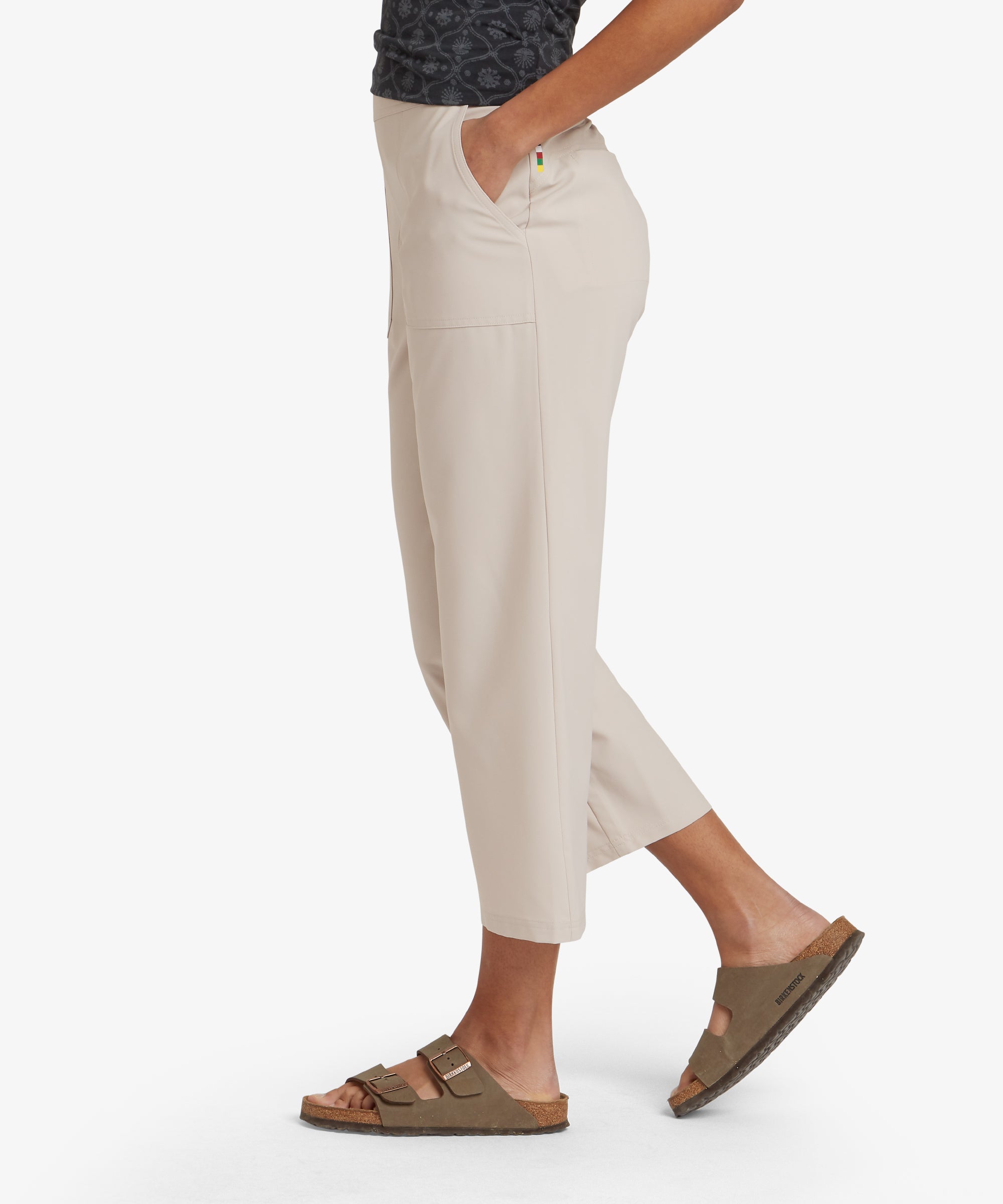 A side view of the model in Sherpa Adventure Gear Sajilo Capri in Beige, showing the straight-leg cut and comfortable fit. One hand is casually placed in the pocket, highlighting the relaxed and practical design of the pants