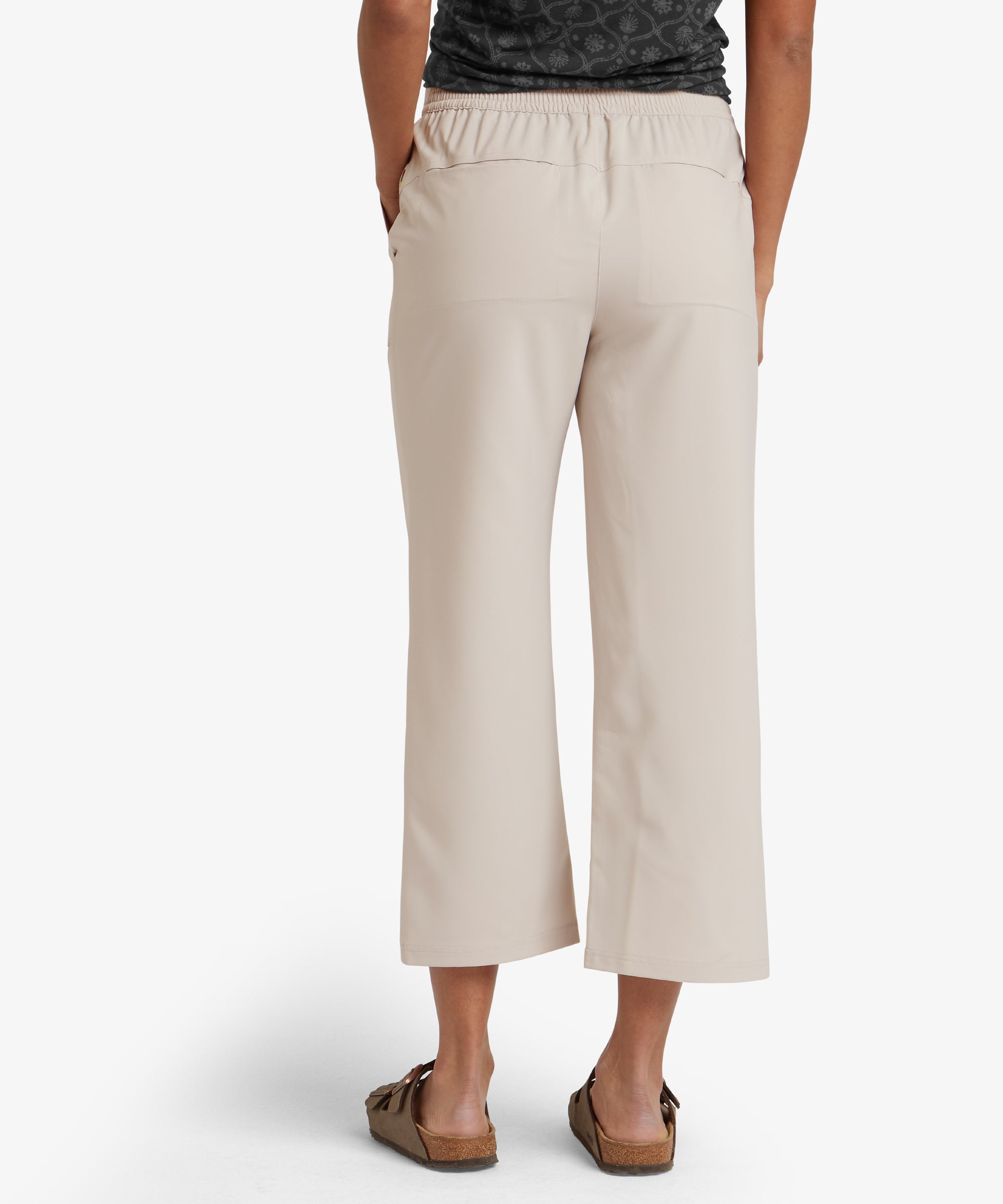 A rear view of the model wearing the Sherpa Adventure Gear Sajilo Capri in Beige, showcasing the smooth back design. The pants fit snugly around the waist and hips and feature a slightly elastic waistband for comfort.