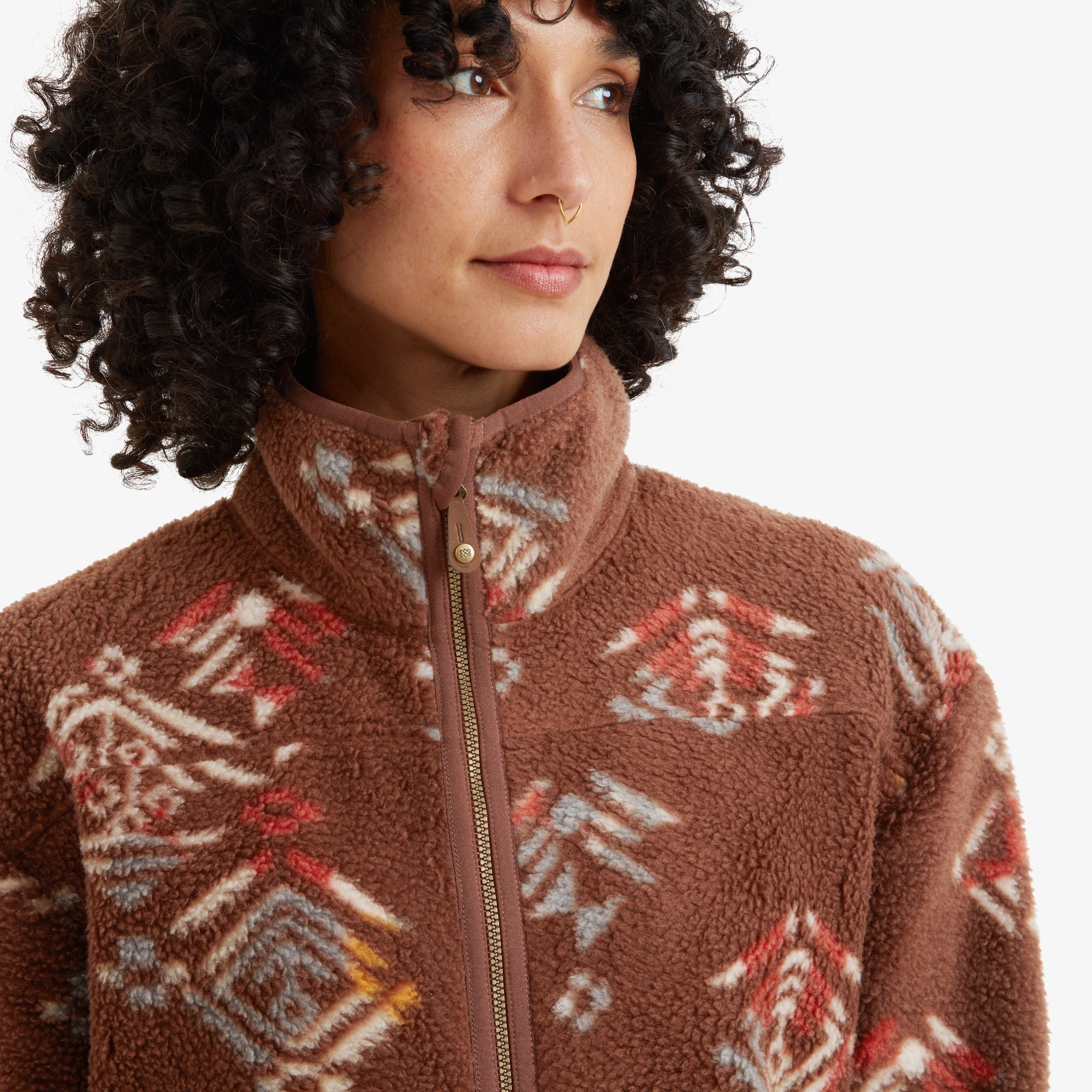 A detailed view of the Sherpa Adventure Gear Uddesya Eco Jacket in Brown's high collar and zippered closure. The colorful geometric design is displayed prominently on the fleece texture, with the zipper featuring a small branded pull tab.