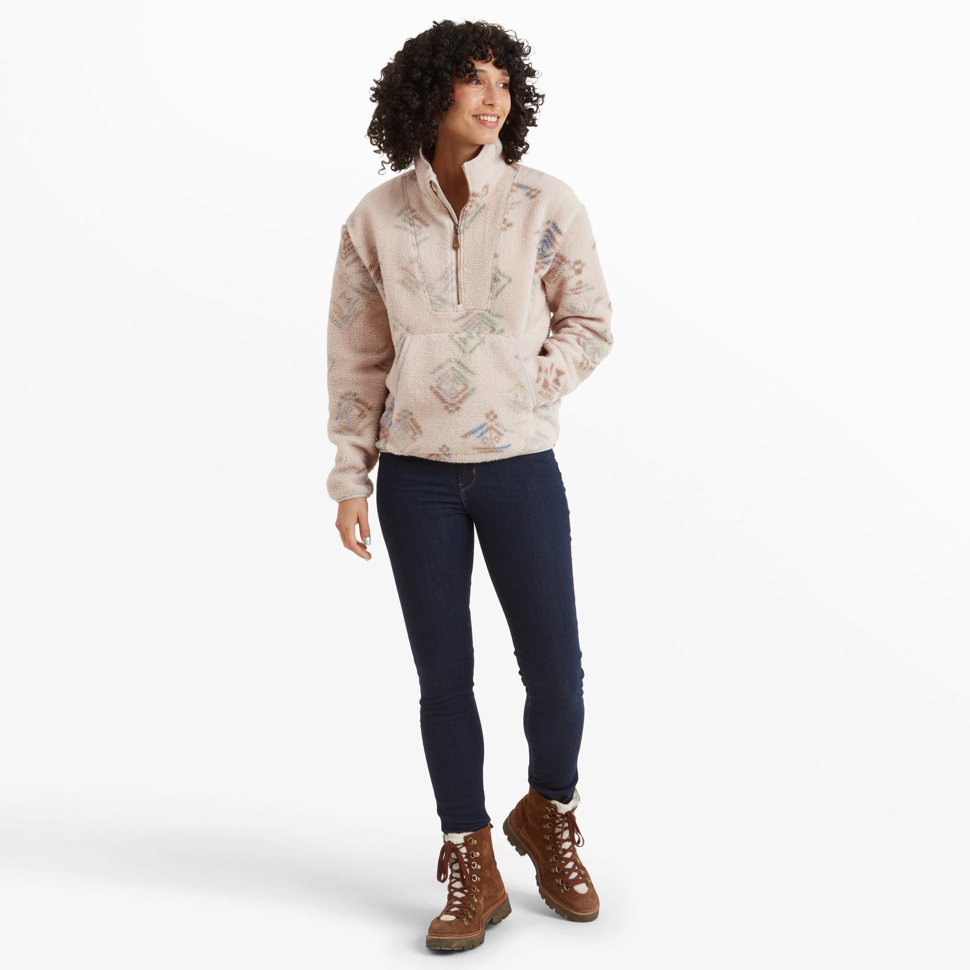 The model showcases the complete outfit, wearing the Sherpa Adventure Gear Uddesya Eco Quarter Zip Jacket in Light Brown with the zipper slightly undone for a relaxed appearance. The dark denim jeans and brown lace-up boots complement the light beige jacket, emphasising an outdoor, cold-weather style.