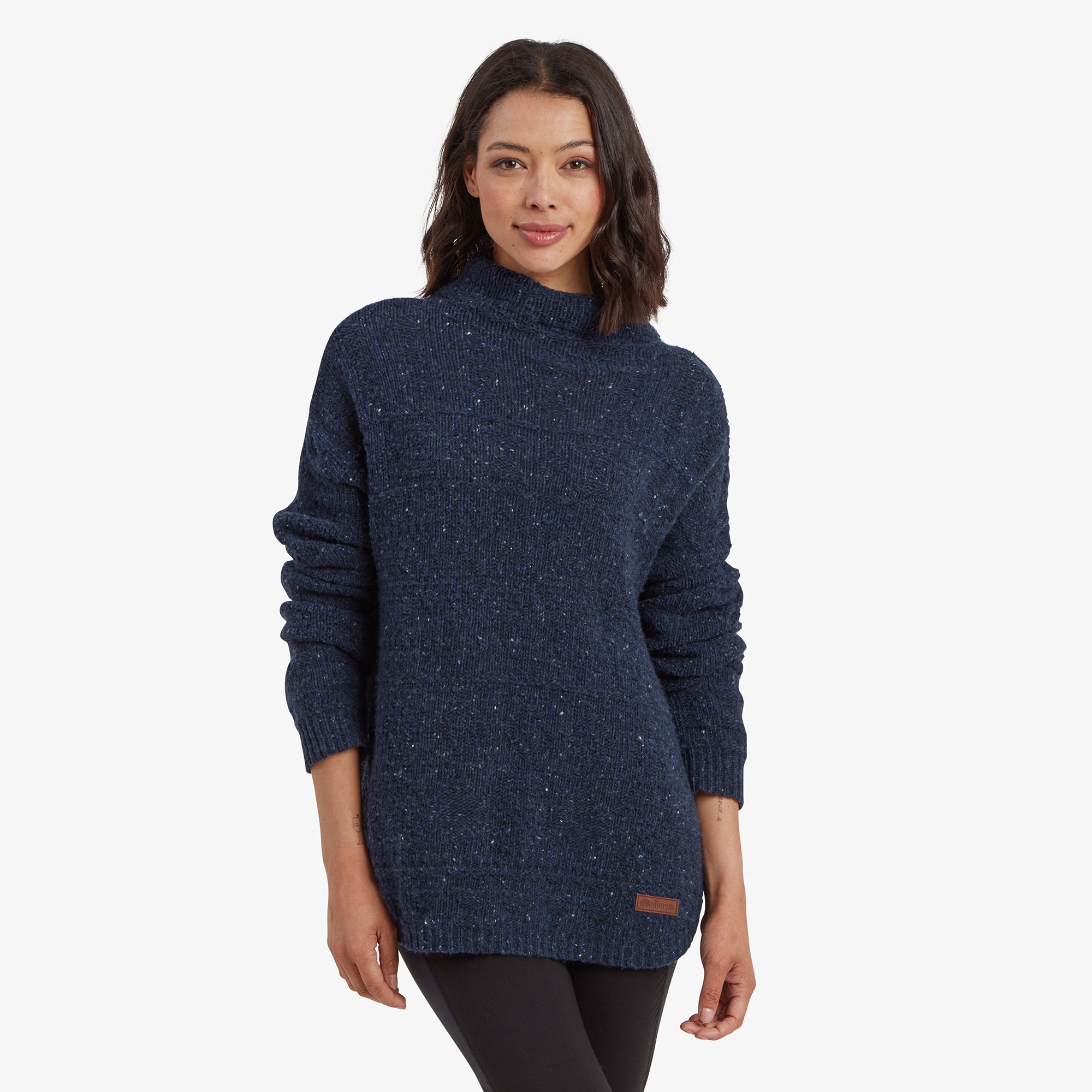 A front view of a woman wearing a Sherpa Adventure Gear Yuden Pullover Sweater in Blue. The sweater has a relaxed fit with a slightly high neckline. The model is paired with black leggings, showcasing the textured fabric with subtle white flecks.